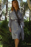 Woman in a blue and black wrap robe with starfish print standing in tropical garden with palm trees