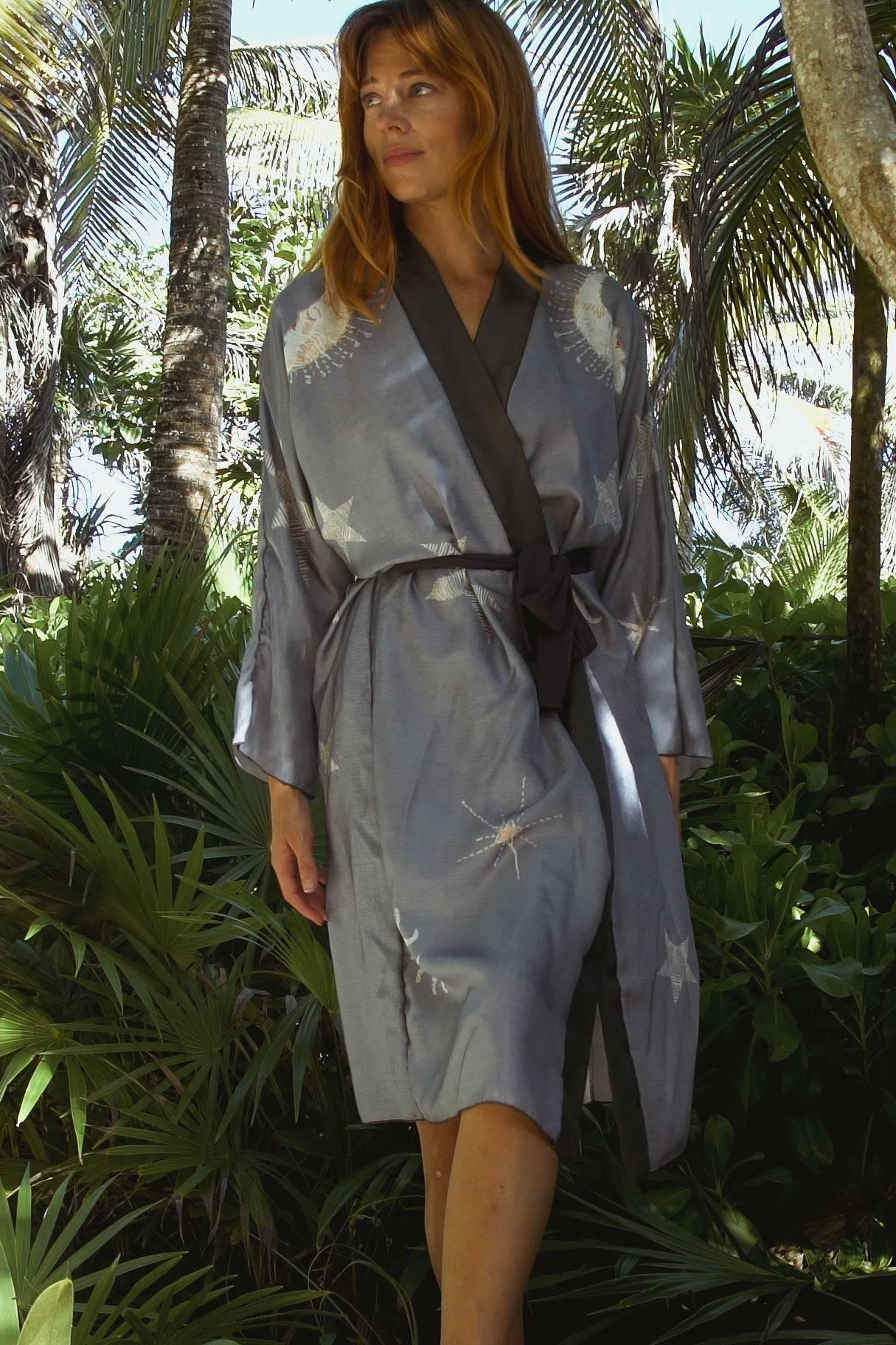 Woman in a blue and black wrap robe with starfish print standing in tropical garden with palm trees