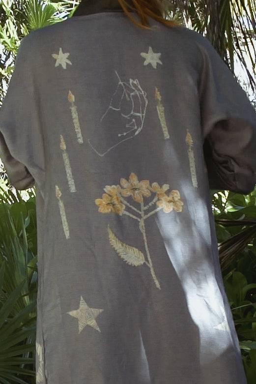 Gray jacket with hand, stars, candles, and floral embroidery design, worn outdoors