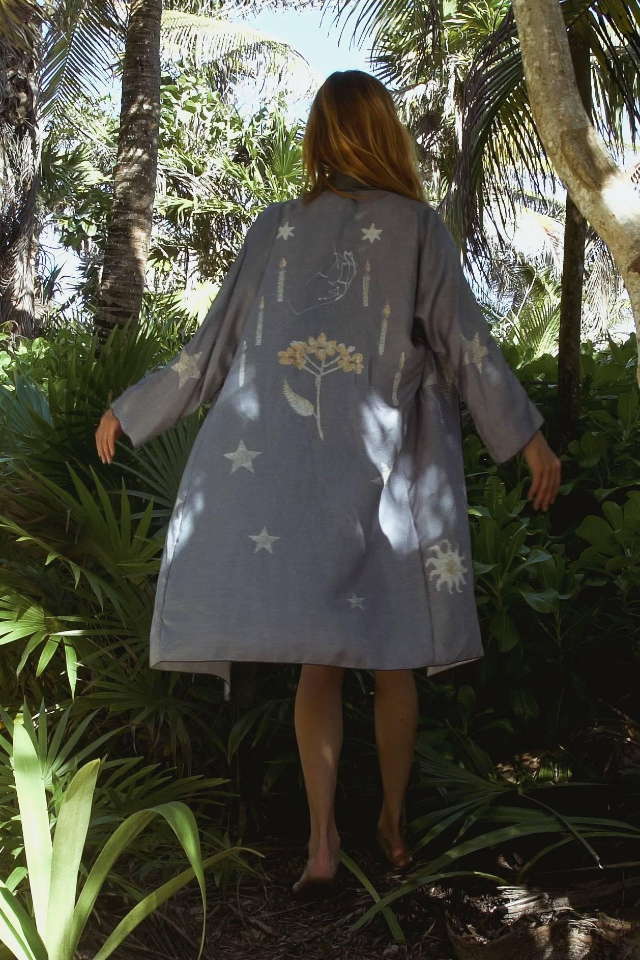 Woman walking barefoot in a lush tropical forest wearing a gray coat with floral and star designs