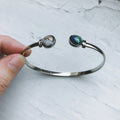 Hand holding silver open bangle bracelet with two gemstone ends, Qu!rk Boutique jewelry