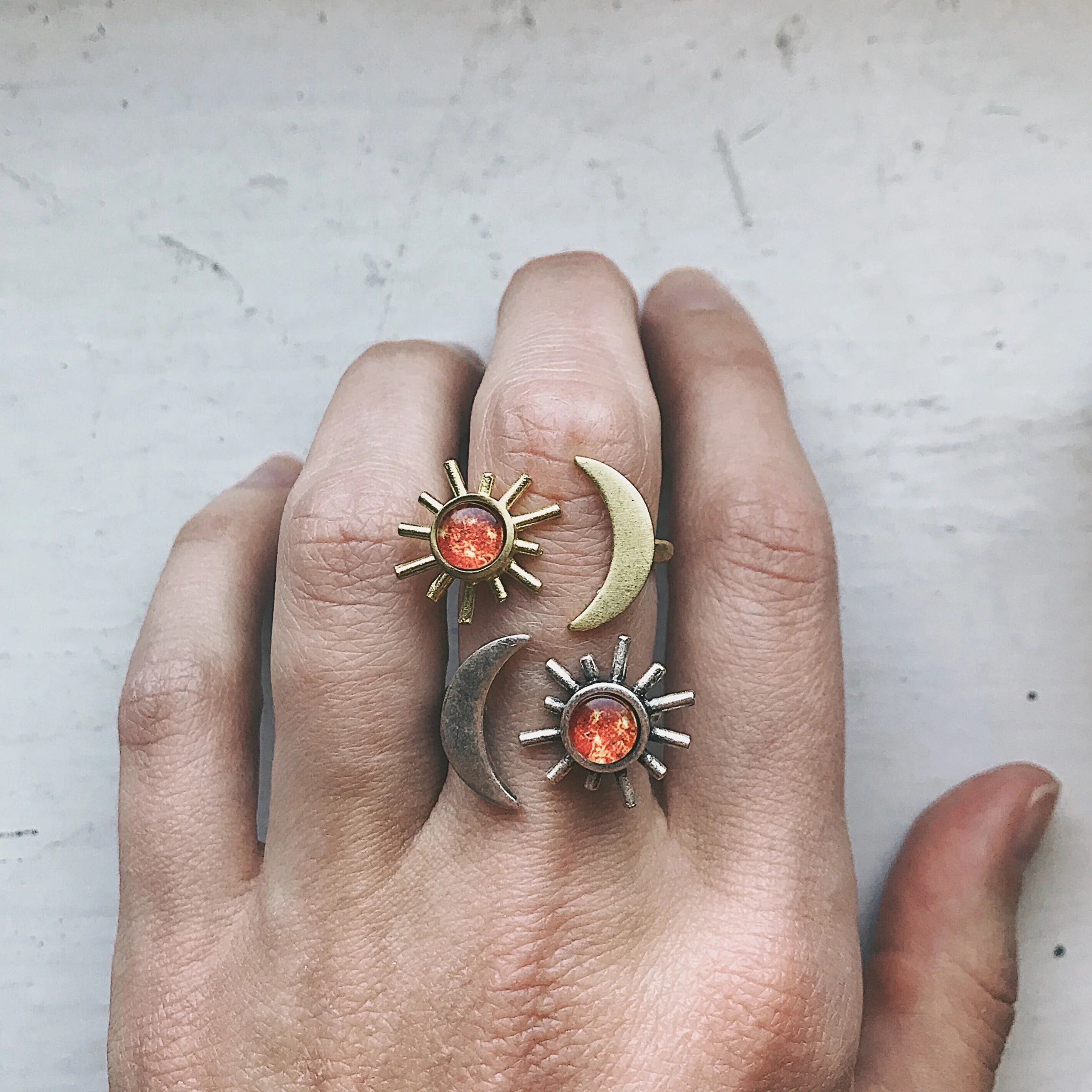 Hand wearing two sun and two moon rings with orange gems on a light surface