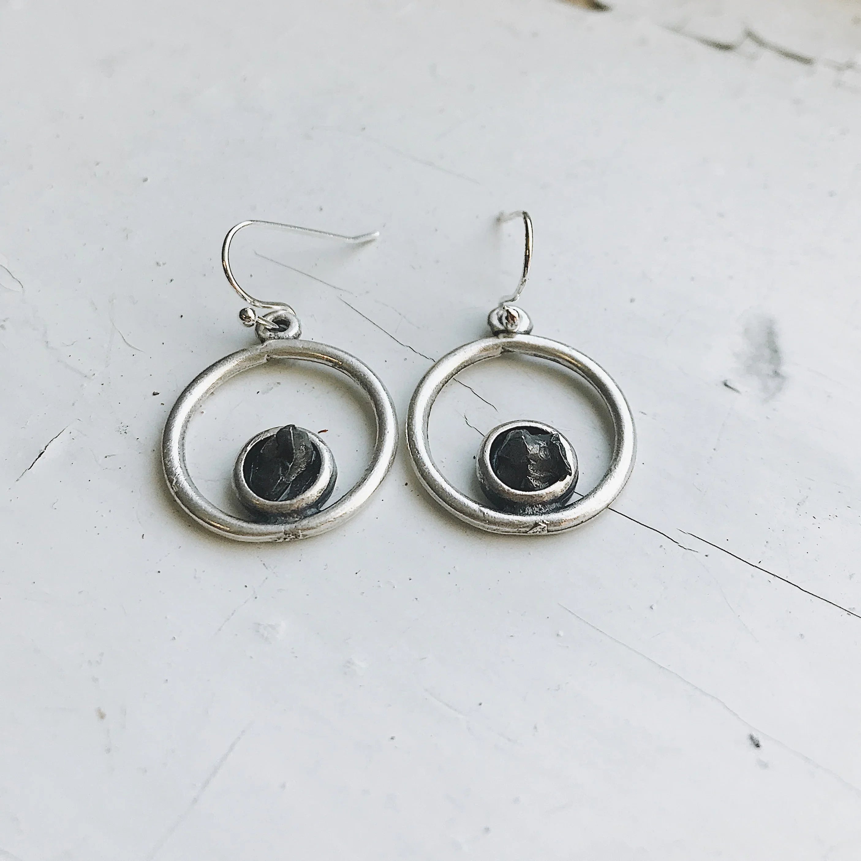 Silver hoop earrings with black textured stone center on white surface