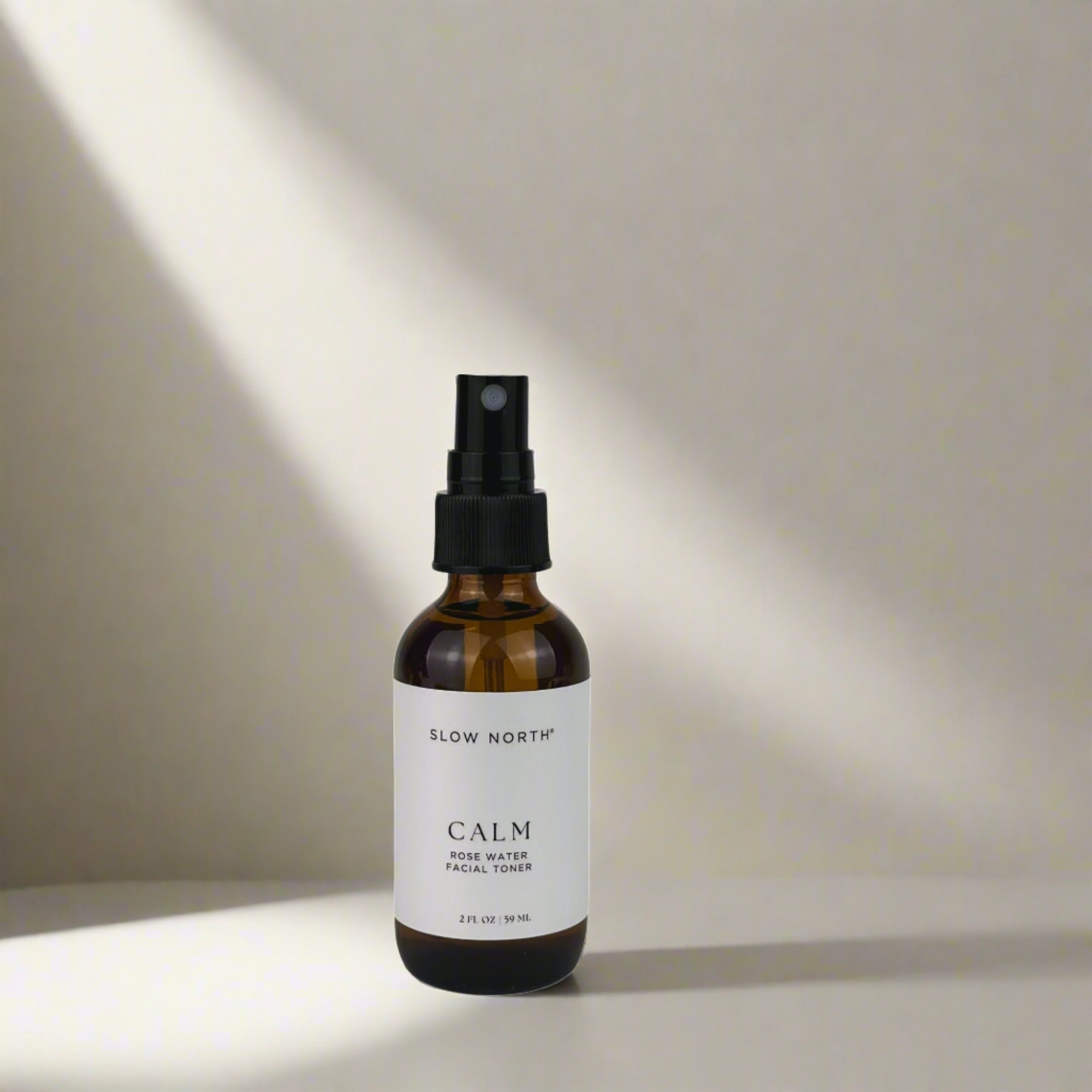 Slow North Calm rose water facial toner in amber spray bottle on neutral background with soft light