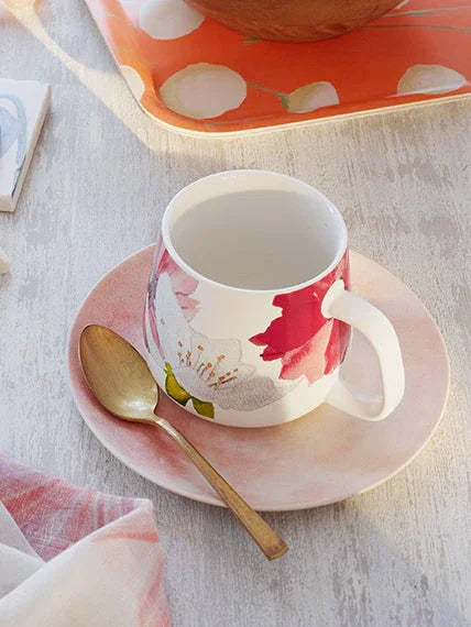 Floral ceramic mug on pink saucer with brass spoon on light wooden table