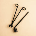 Black metal candle care tool set with wick trimmer and snuffer on beige background