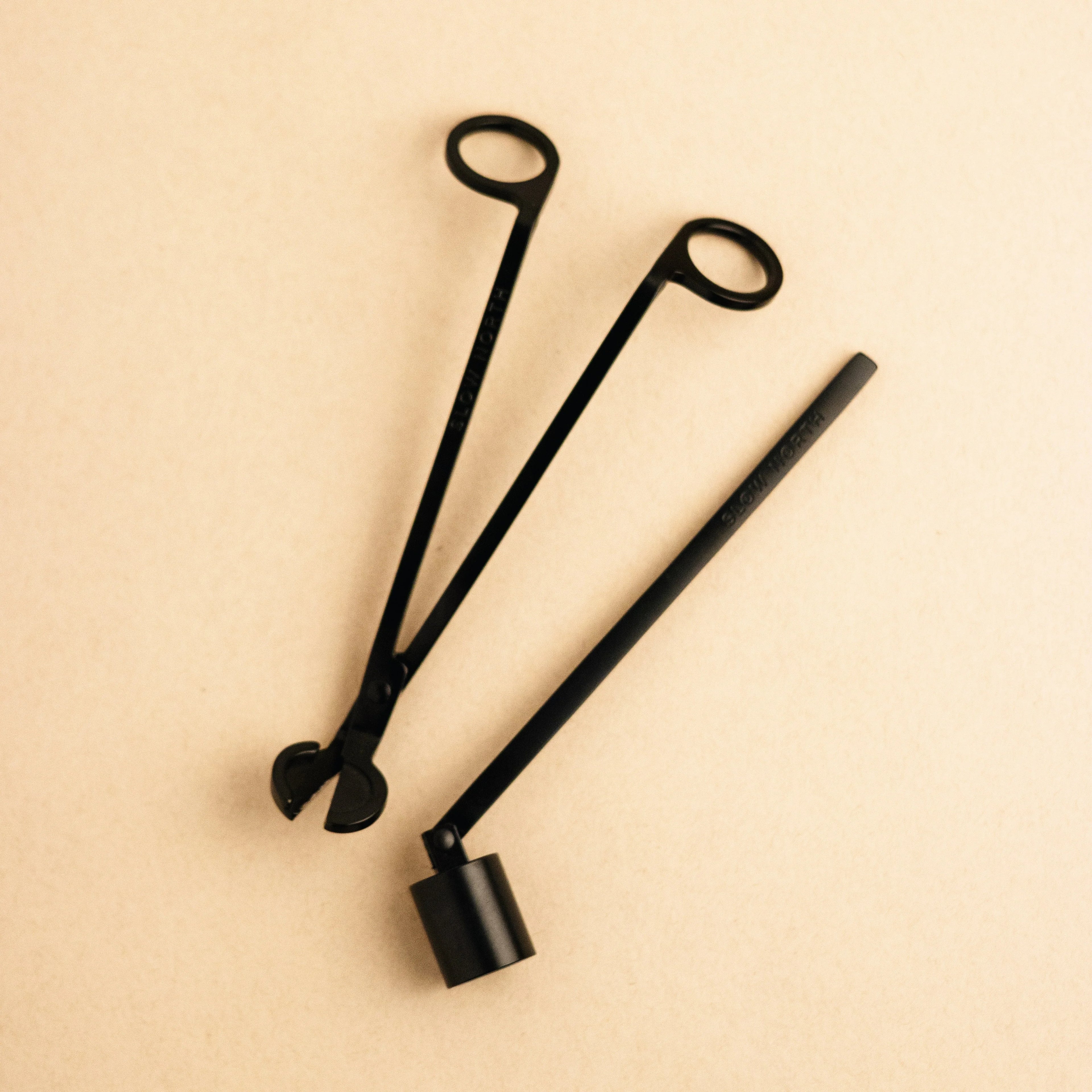 Black metal candle care tool set with wick trimmer and snuffer on beige background