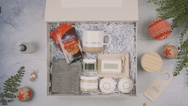 Christmas gift box with cozy mug, coffee packets, skincare jars, towel, soap, and festive decorations