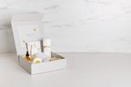 Open white gift box with honey-themed skincare products including jars, bottles, and bars on a light marble background
