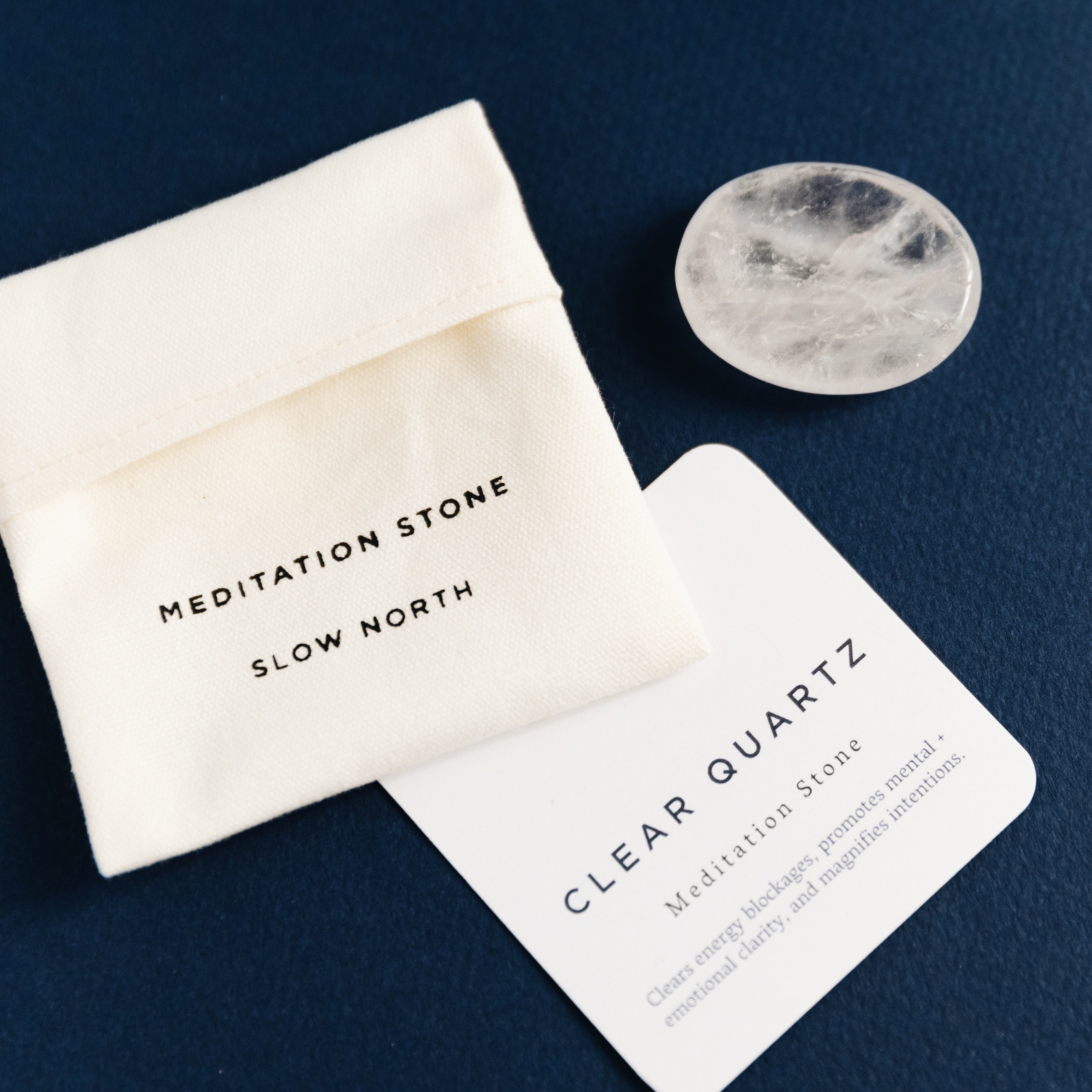 Clear quartz meditation stone with white pouch labeled Slow North and informational card on navy background