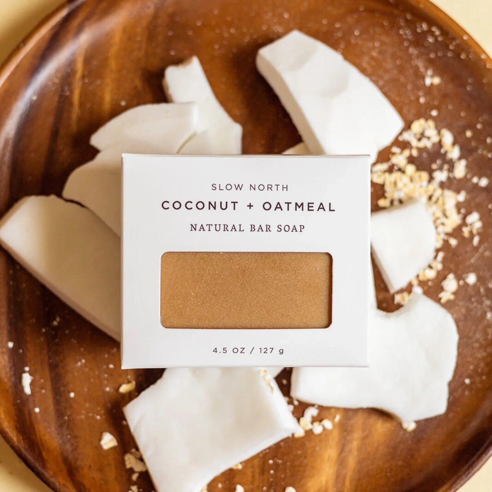 Slow North Coconut + Oatmeal natural bar soap on wooden plate with coconut pieces and oats