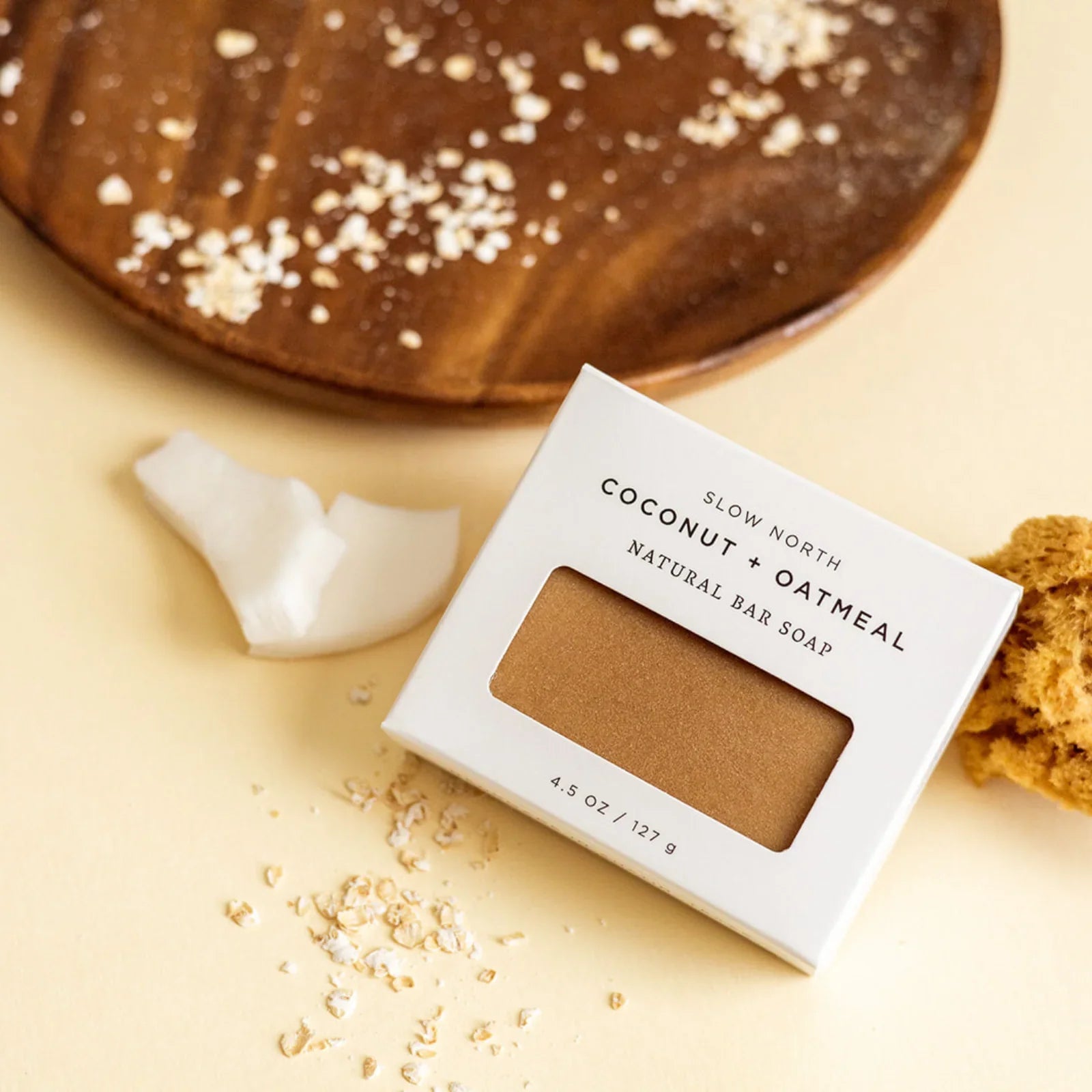 Slow North Coconut + Oatmeal natural bar soap with oatmeal flakes, coconut pieces, and sponge on beige surface