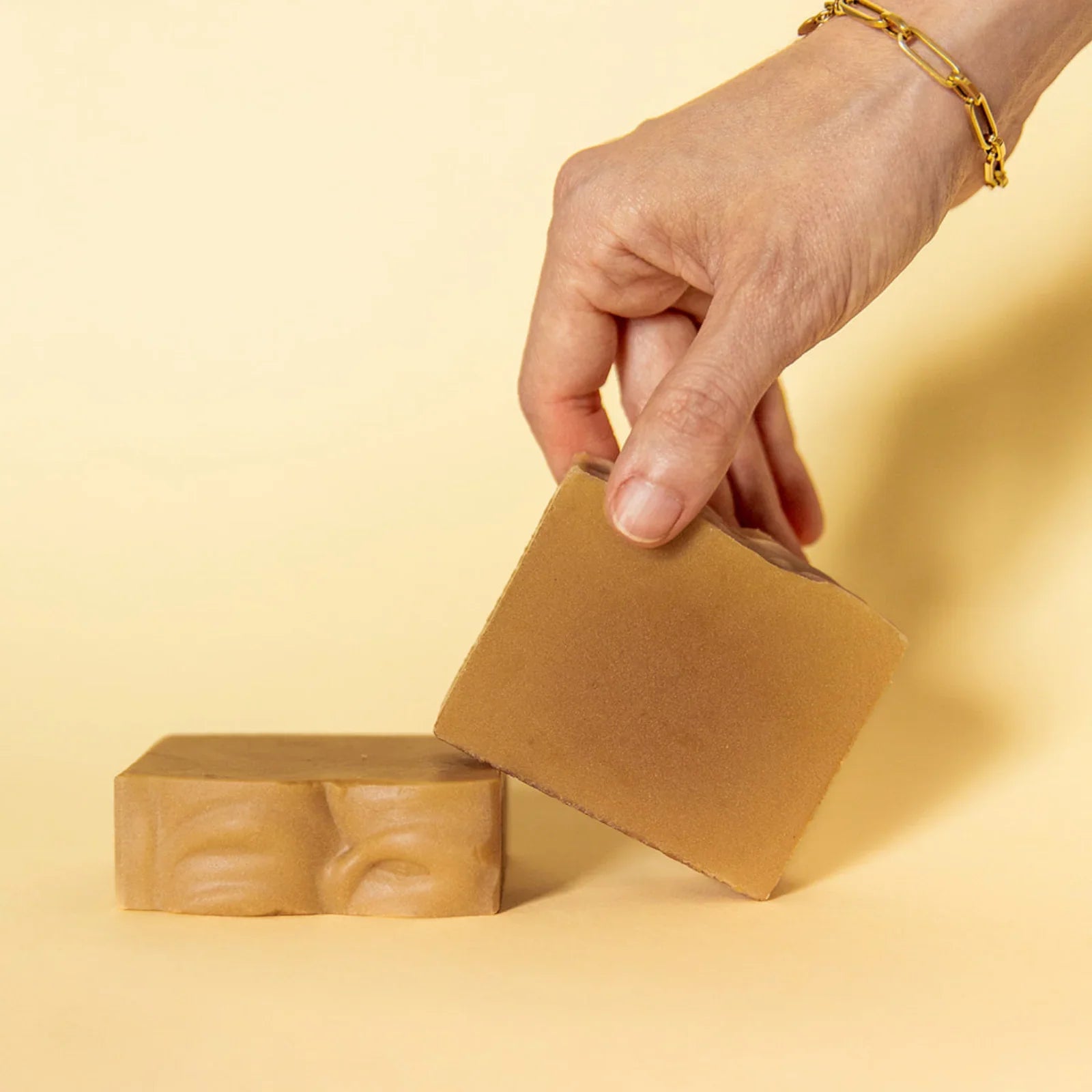 Hand holding brown natural soap bar with another soap bar on beige background