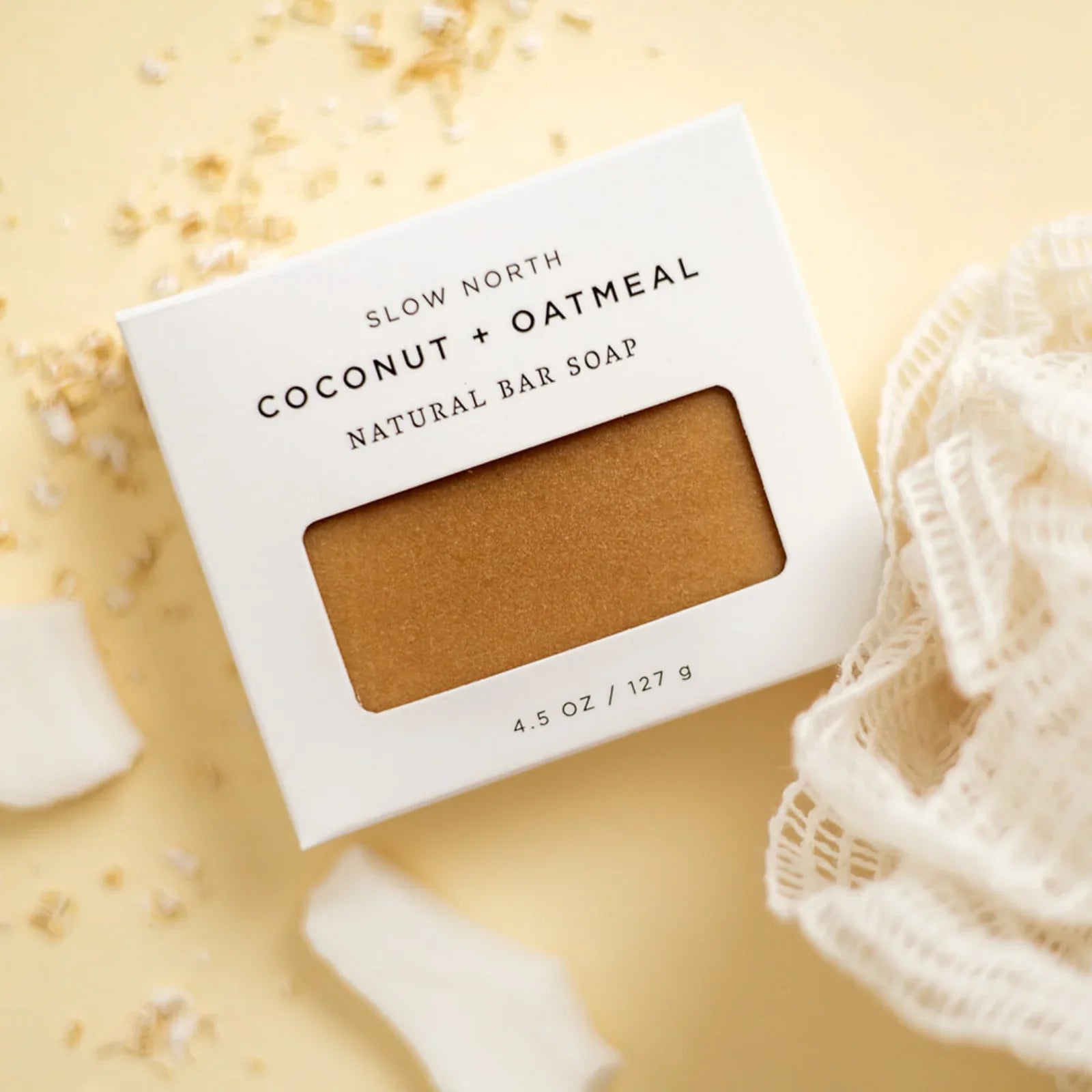 Slow North Coconut + Oatmeal natural bar soap in white box with soap visible, cotton cloth, and scattered oats