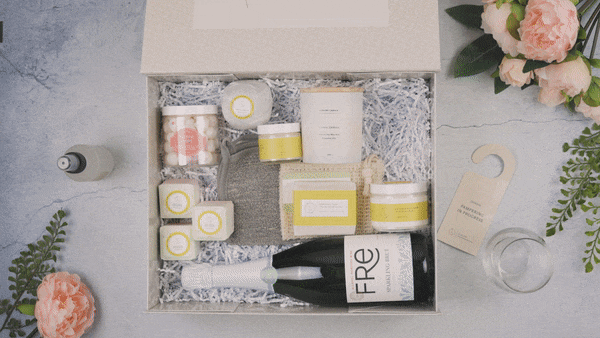 Luxury celebration gift box with sparkling wine, candles, bath salts, soap, cozy socks, and flowers