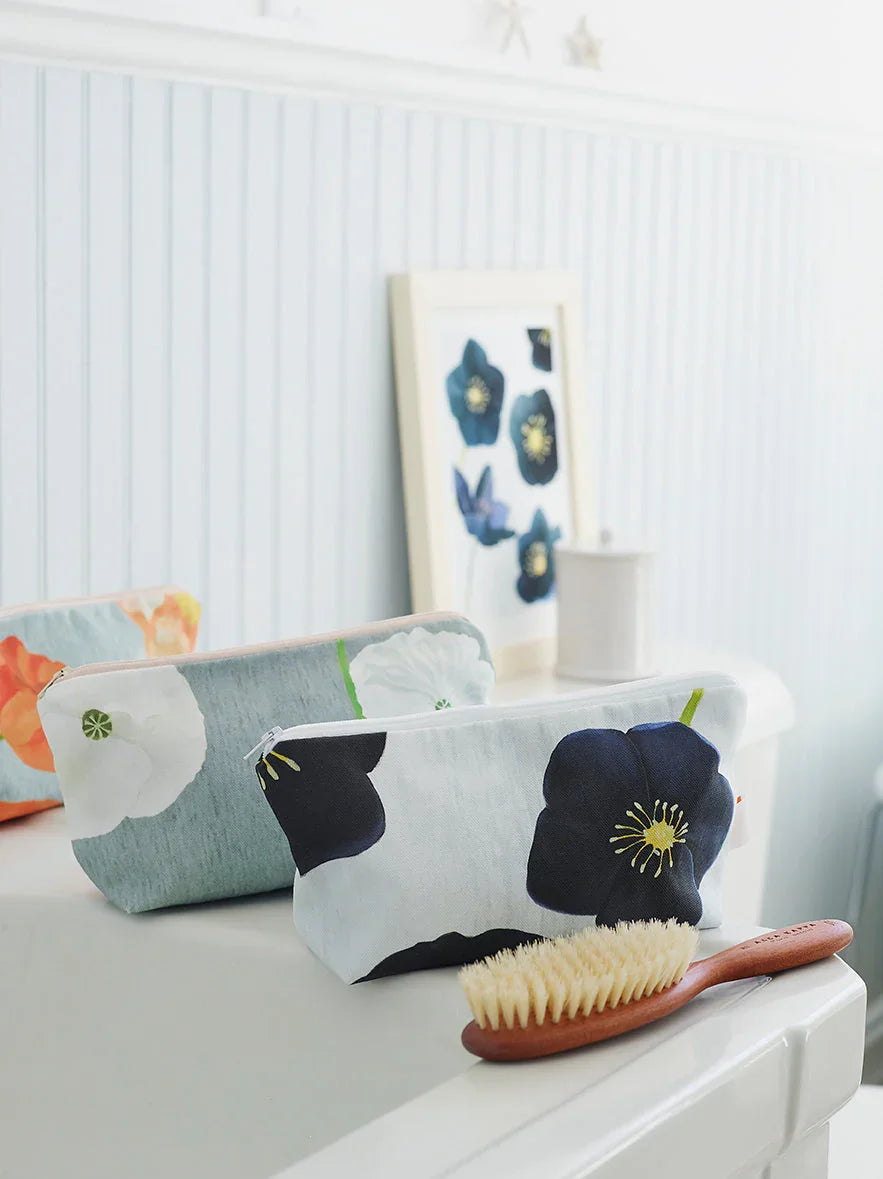 Floral cosmetic bags and wooden hairbrush on white table with framed flower art in light blue room