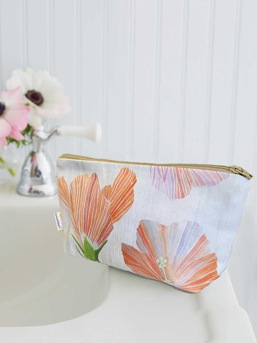 Floral print cosmetic bag with orange and pink flowers placed on white bathroom sink