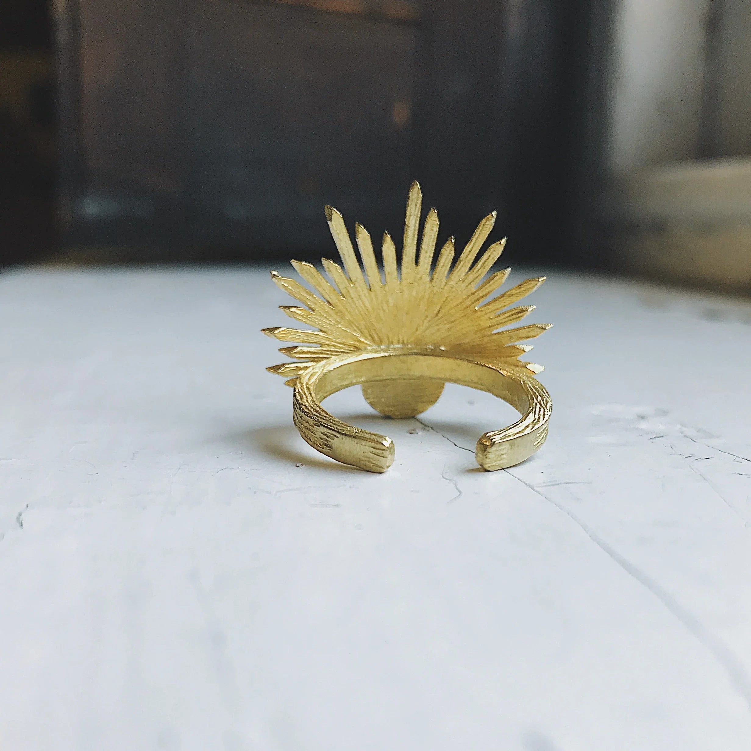 gold sunburst design open ring on rustic white wooden surface