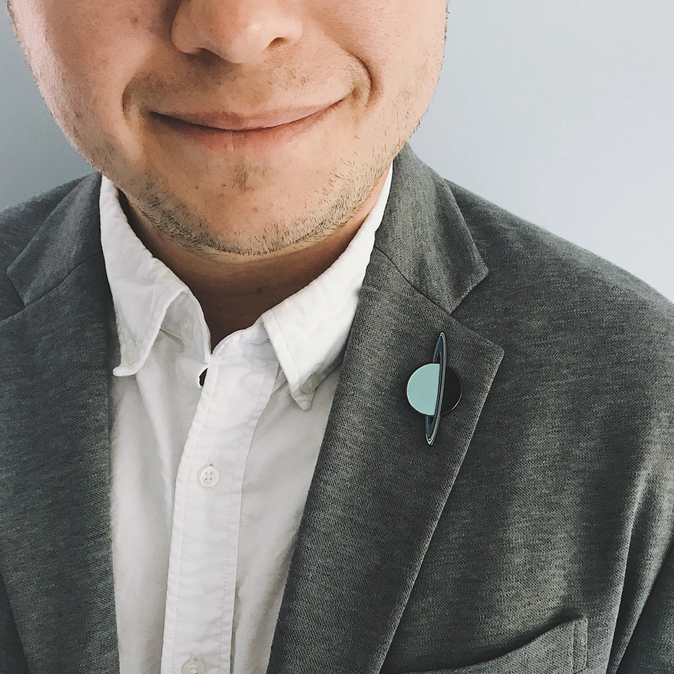 Close-up of man in grey blazer and white shirt wearing planet-shaped enamel lapel pin