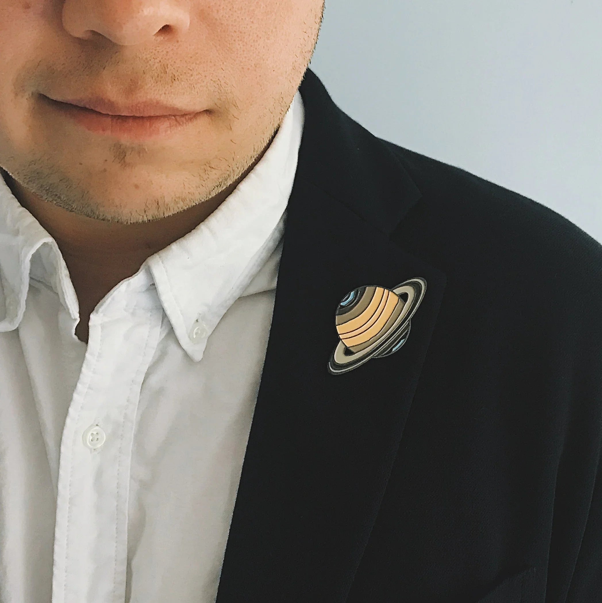 Close-up of man wearing black blazer with Saturn planet lapel pin and white shirt