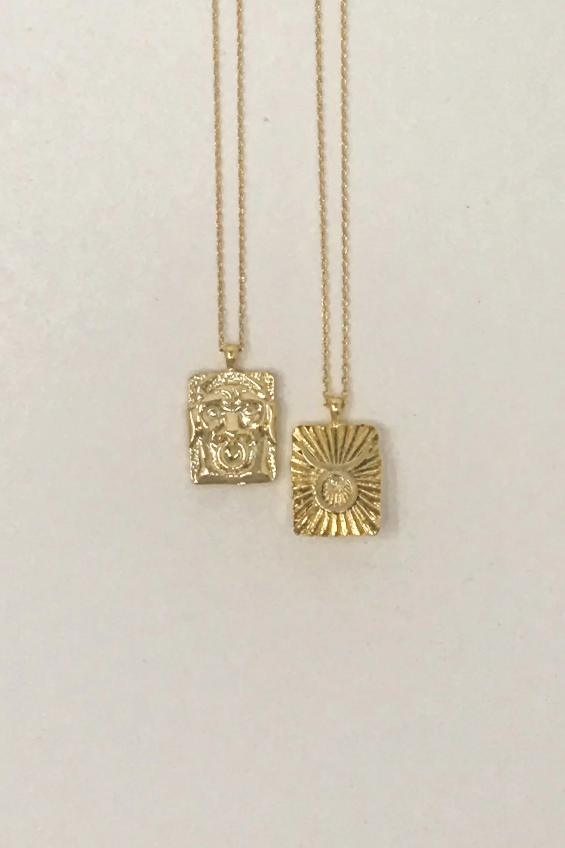 Two gold pendant necklaces with rectangular textured charms on a plain white background