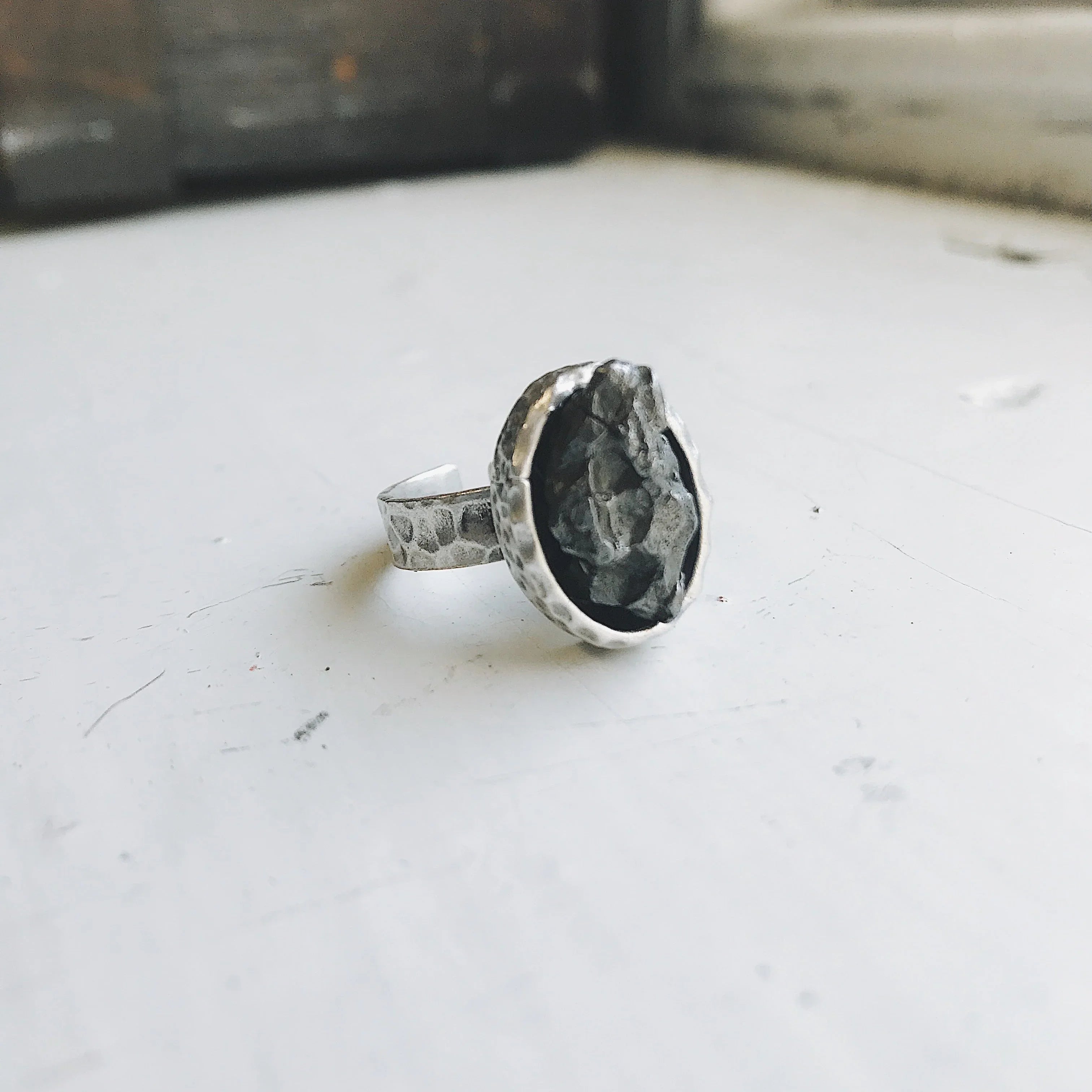 Handcrafted textured silver ring with rough dark stone on a white surface