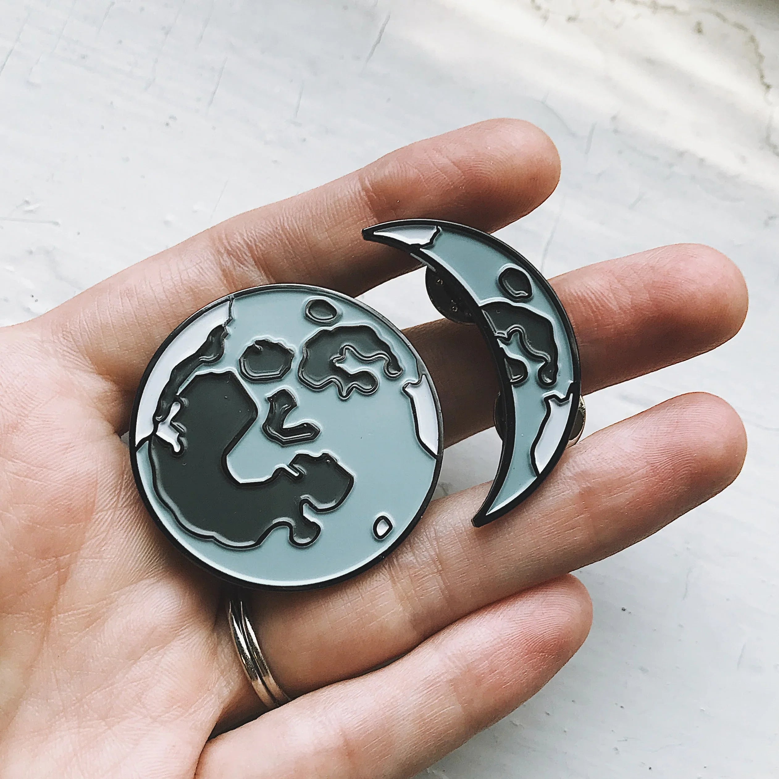 Hand holding two enamel pins featuring a full moon and a crescent moon design