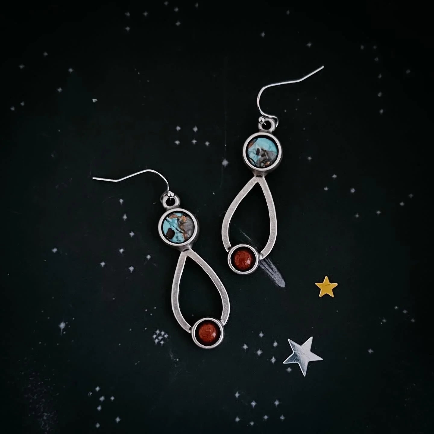 Silver drop-shaped earrings with turquoise and red stones on black starry background