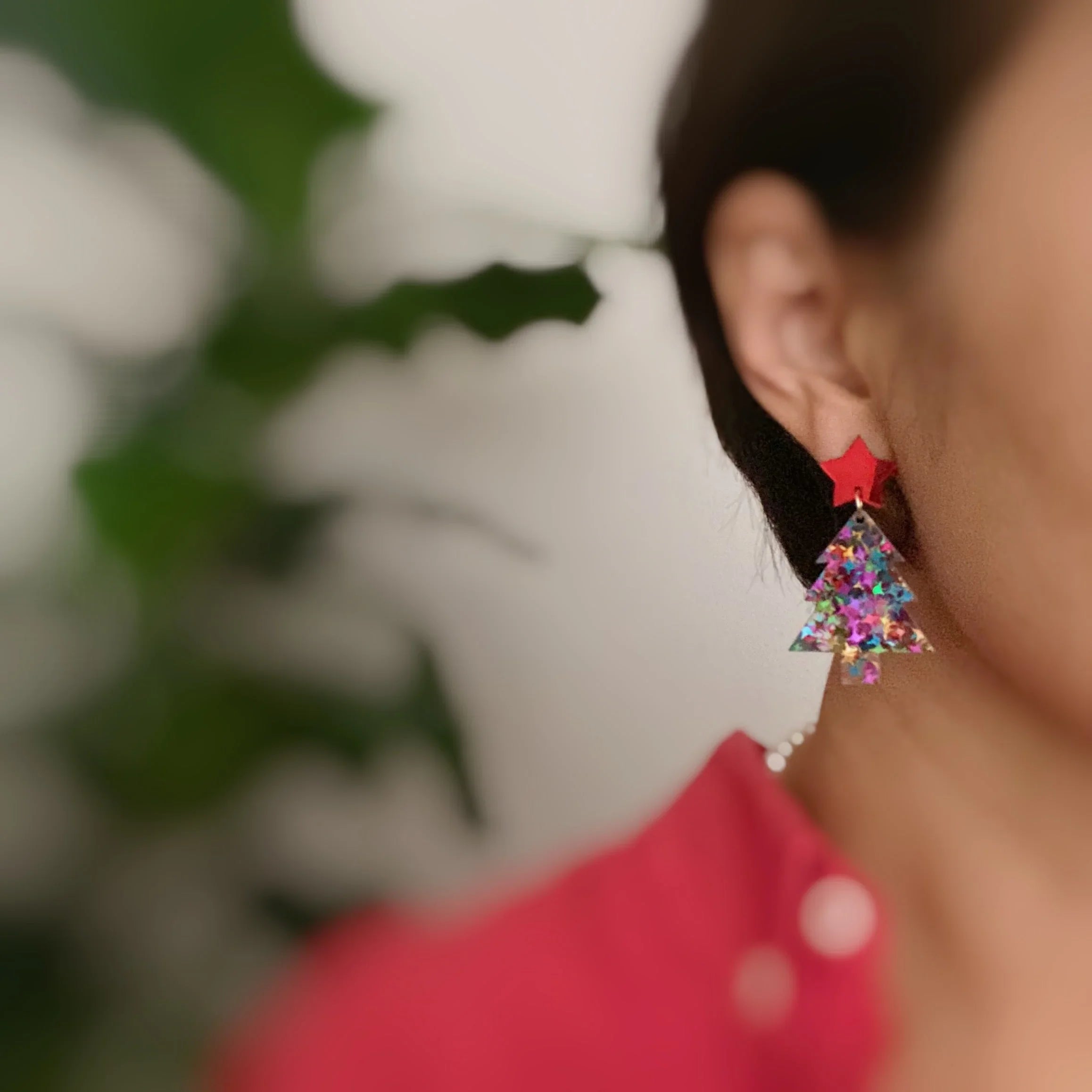 Close-up of person wearing colorful Christmas tree earrings with red star studs and festive outfit