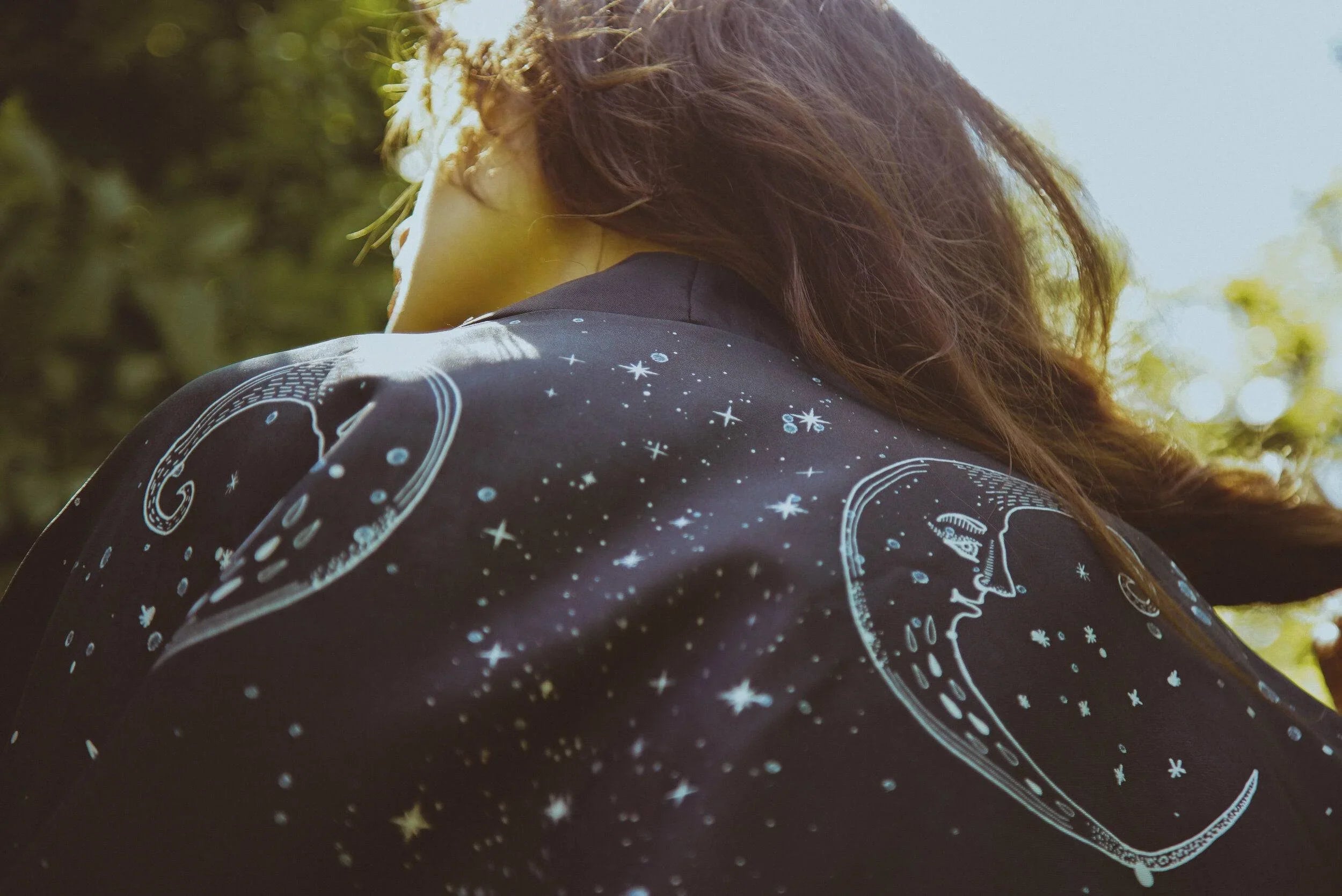 Person wearing black jacket with celestial moon and star designs in outdoor natural light