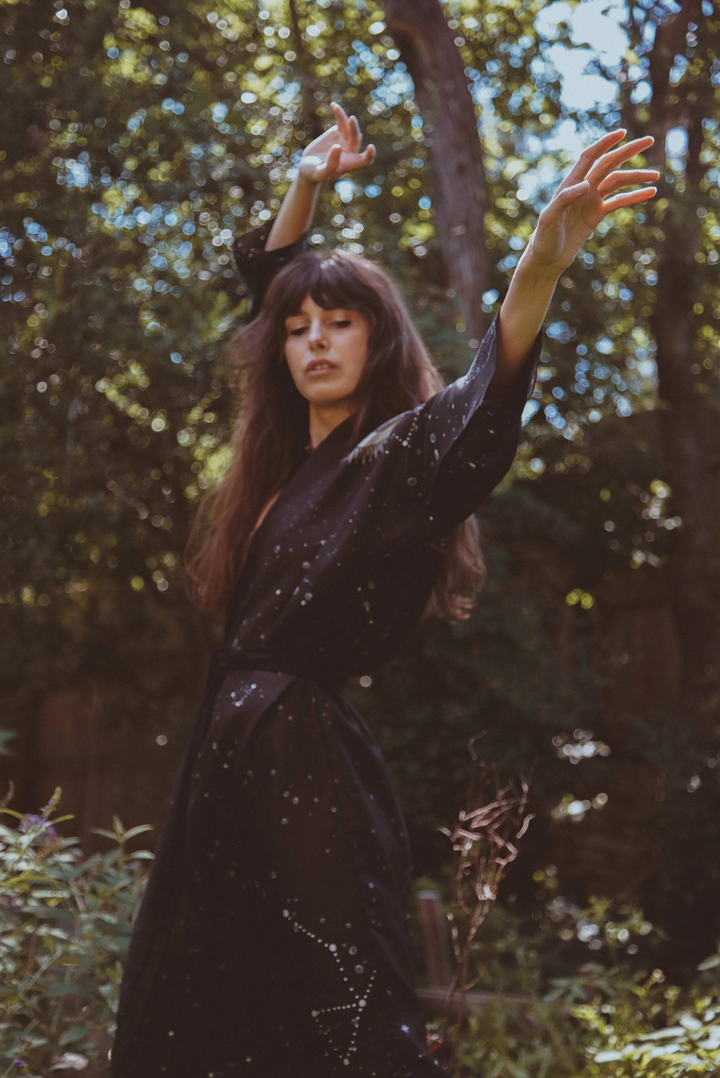 Woman in a black starry-patterned robe posing gracefully outdoors in a sunlit forest