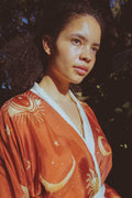 Young woman with curly hair wearing rust-orange celestial robe with sun and moon patterns in natural light