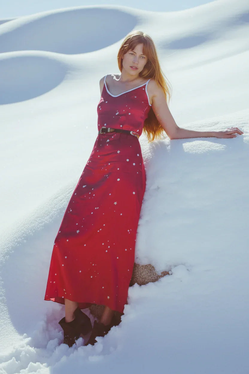 Woman in red polka dot maxi dress and black boots posing in deep snow with smooth snowy background
