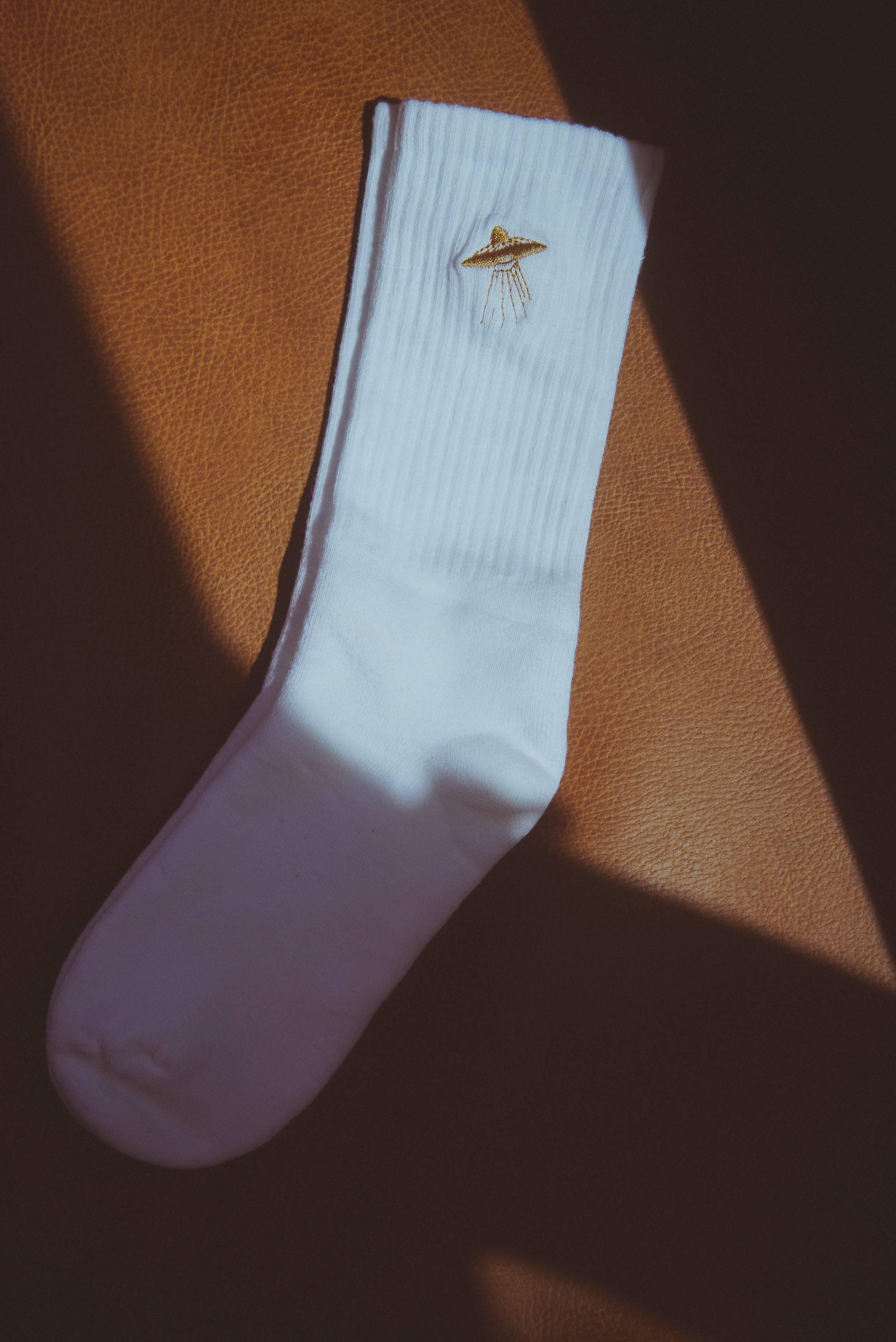 White ribbed sock with gold UFO embroidery on brown leather surface under shadow