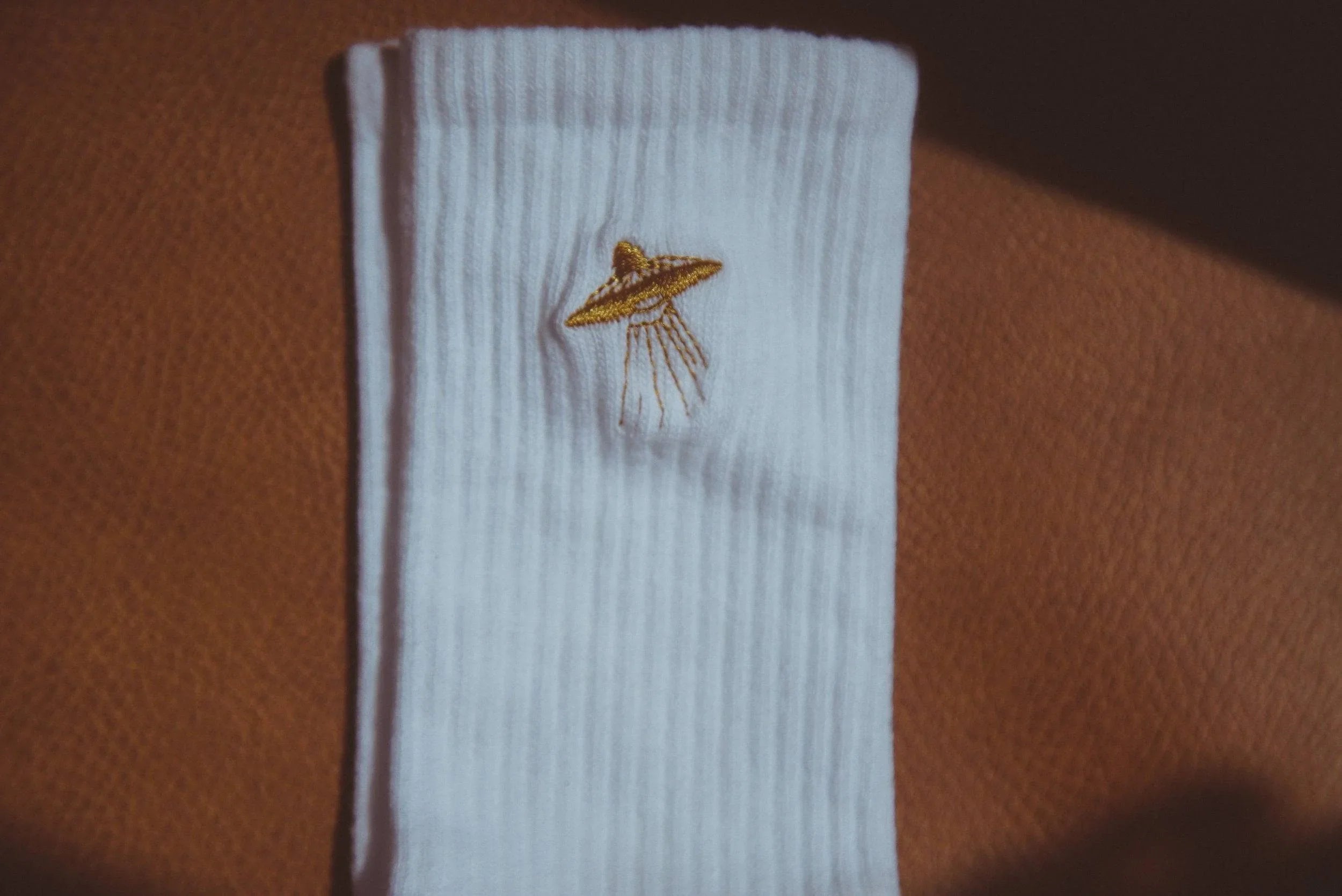 Folded white ribbed sock with embroidered golden UFO design on brown textured surface
