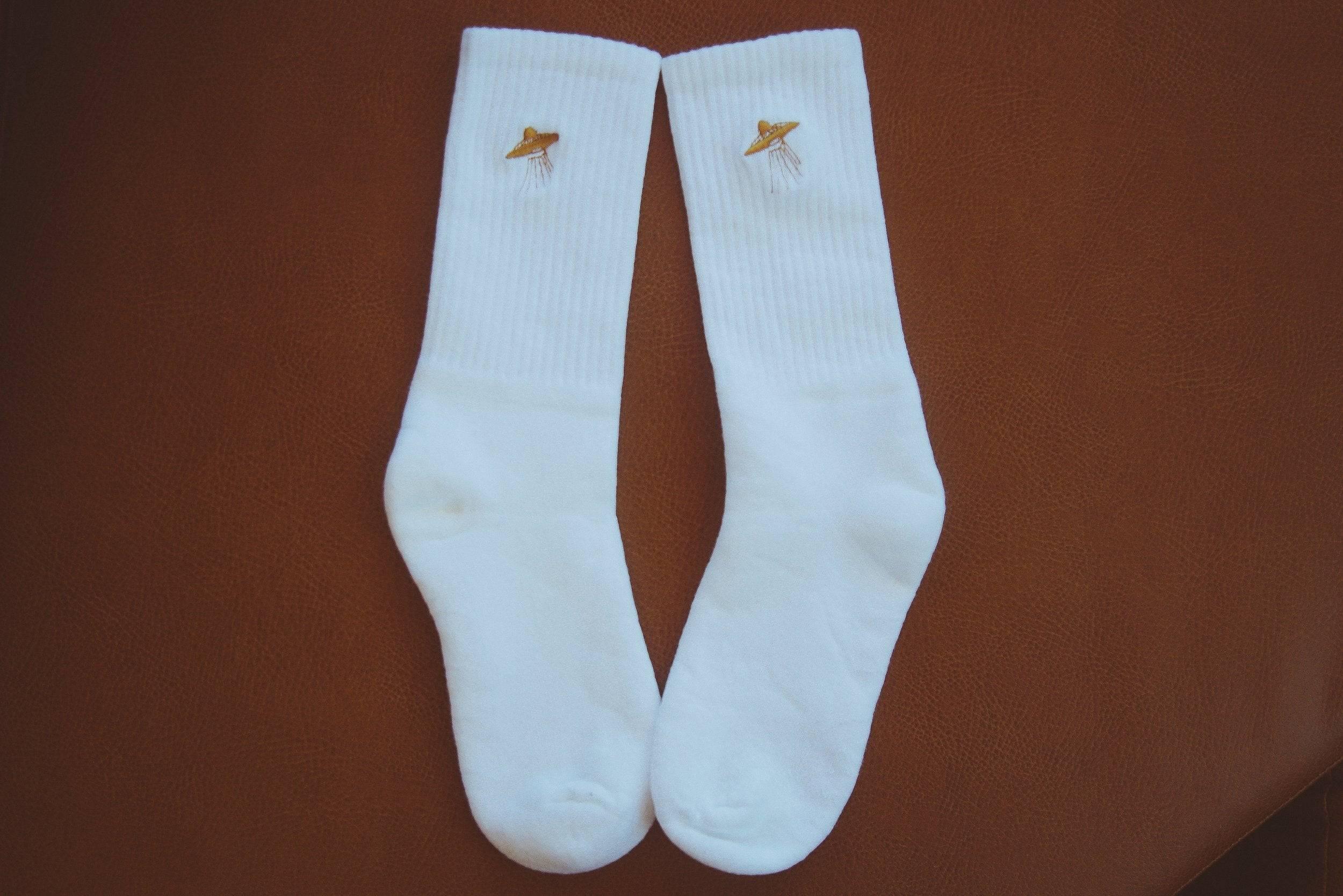 Pair of white crew socks with embroidered yellow UFO design on brown surface