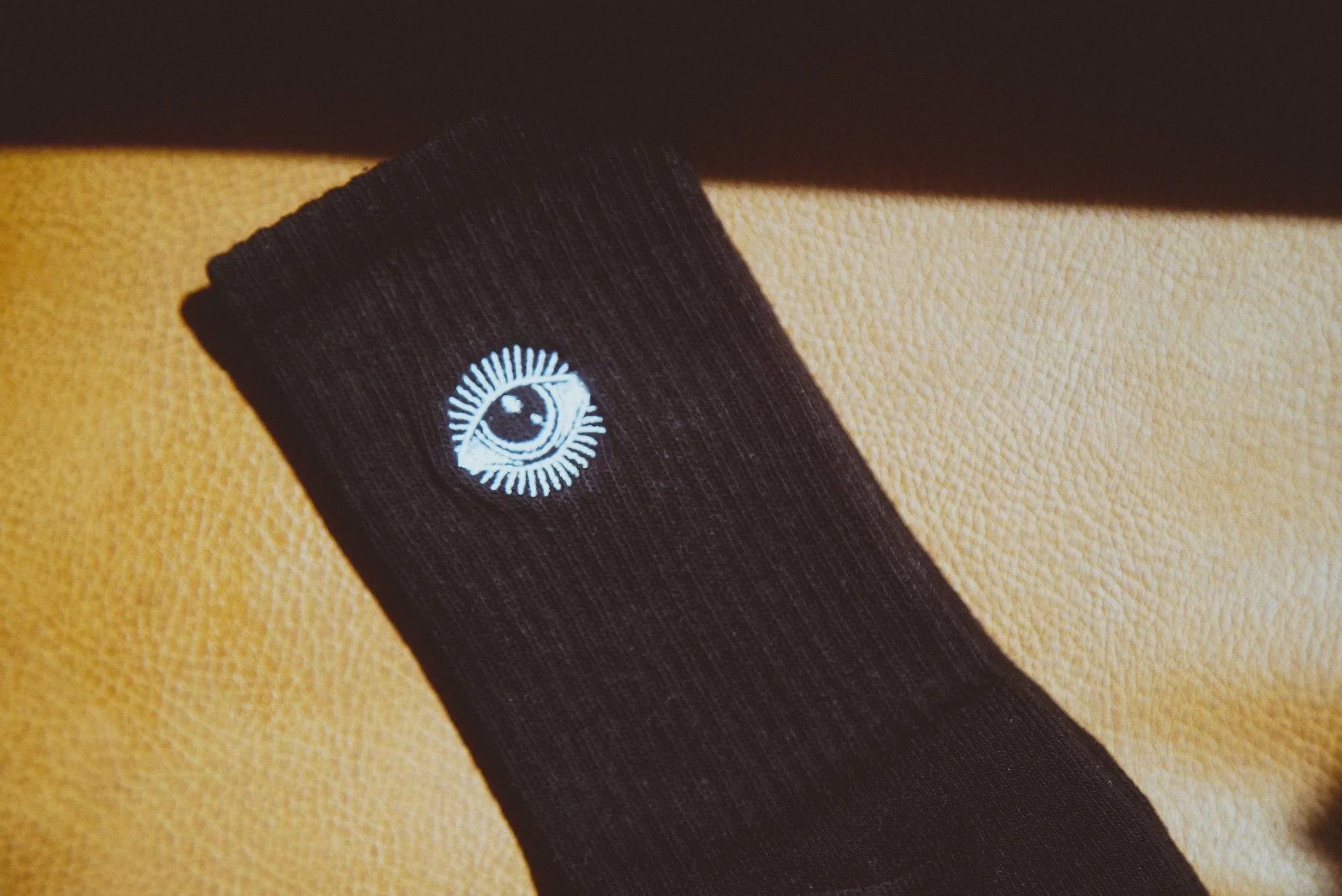 Black ribbed sock with white eye embroidery on tan leather surface