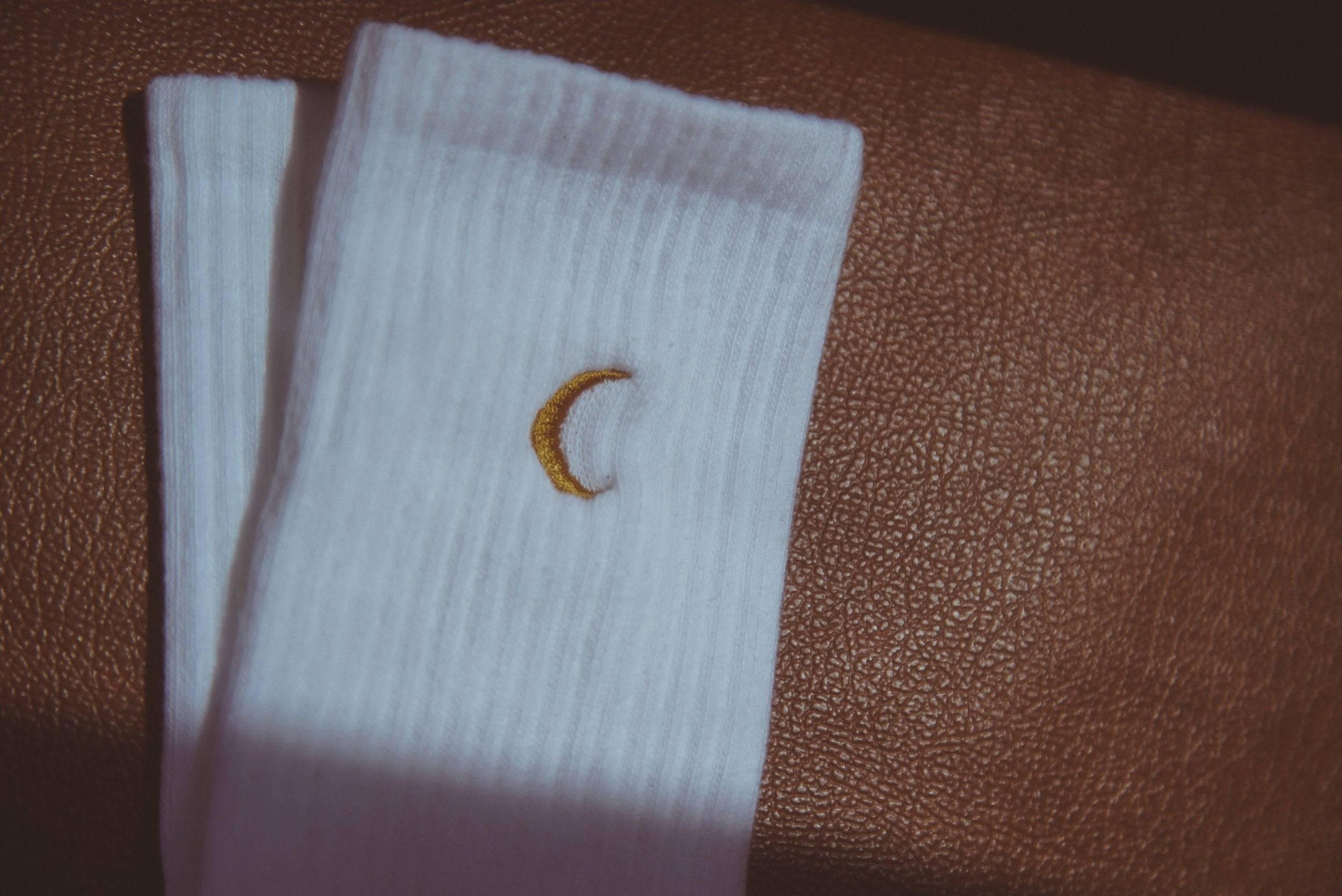 White ribbed socks with small yellow crescent moon embroidery on brown textured surface