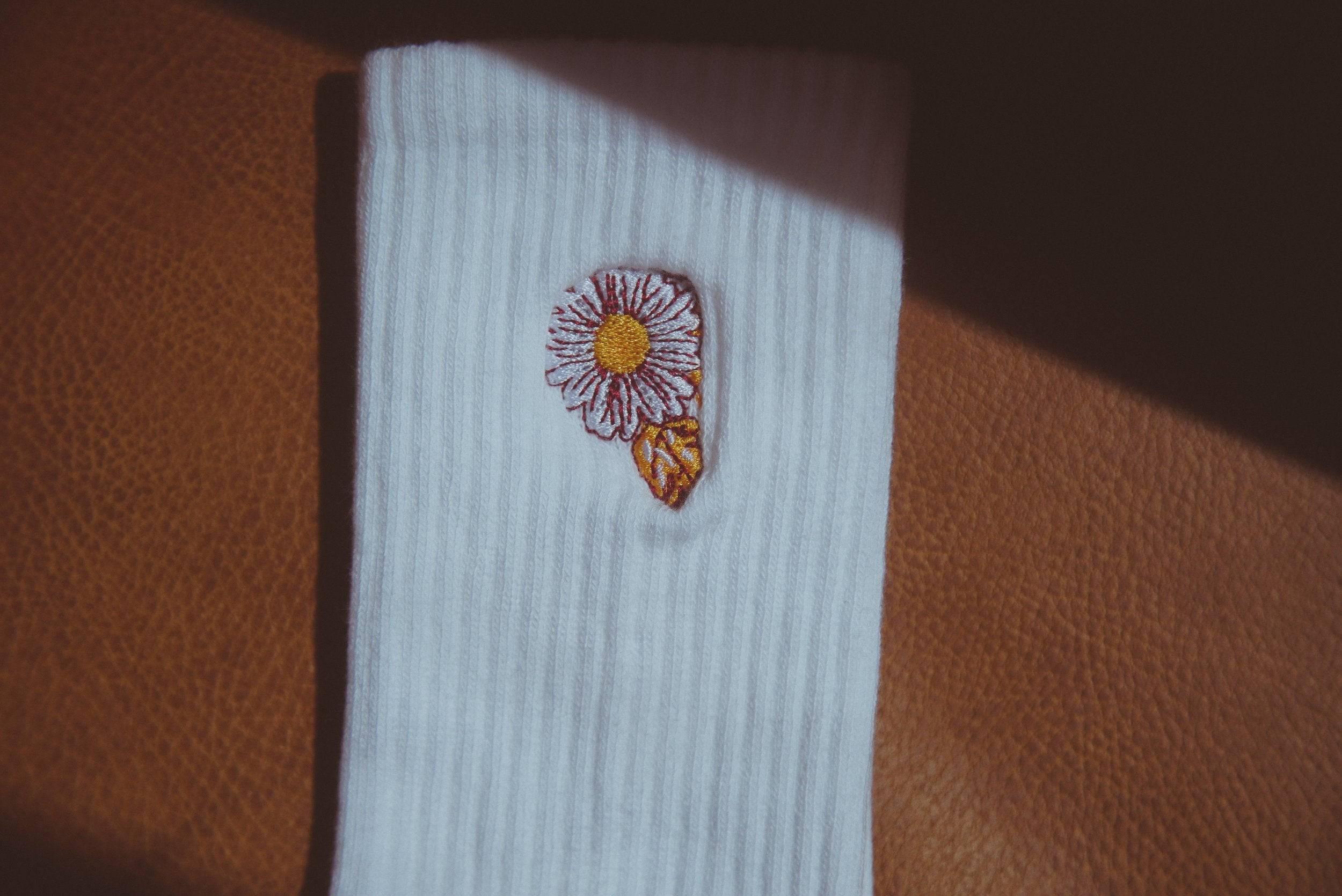 White ribbed sock with embroidered white and yellow flower detail on brown leather surface