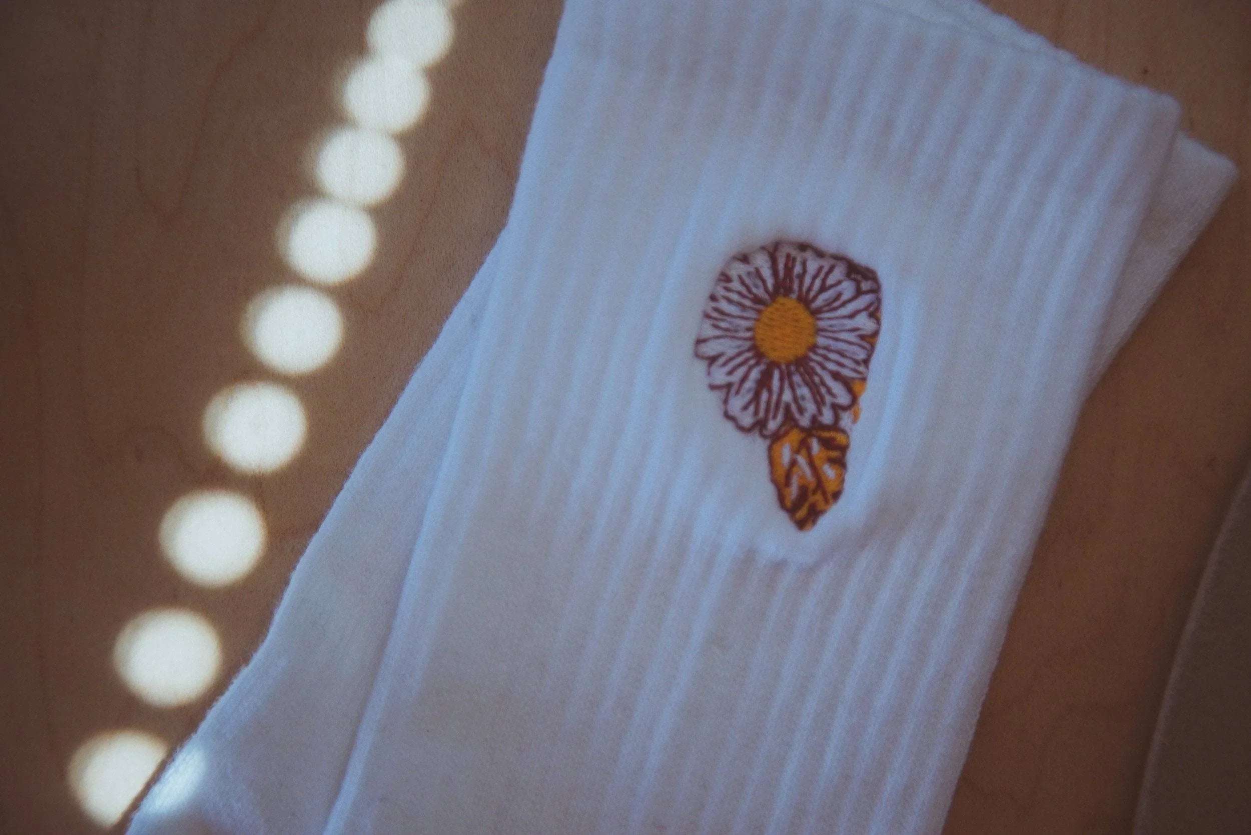 White ribbed socks with embroidered daisy flower and leaf on wooden surface under dotted light