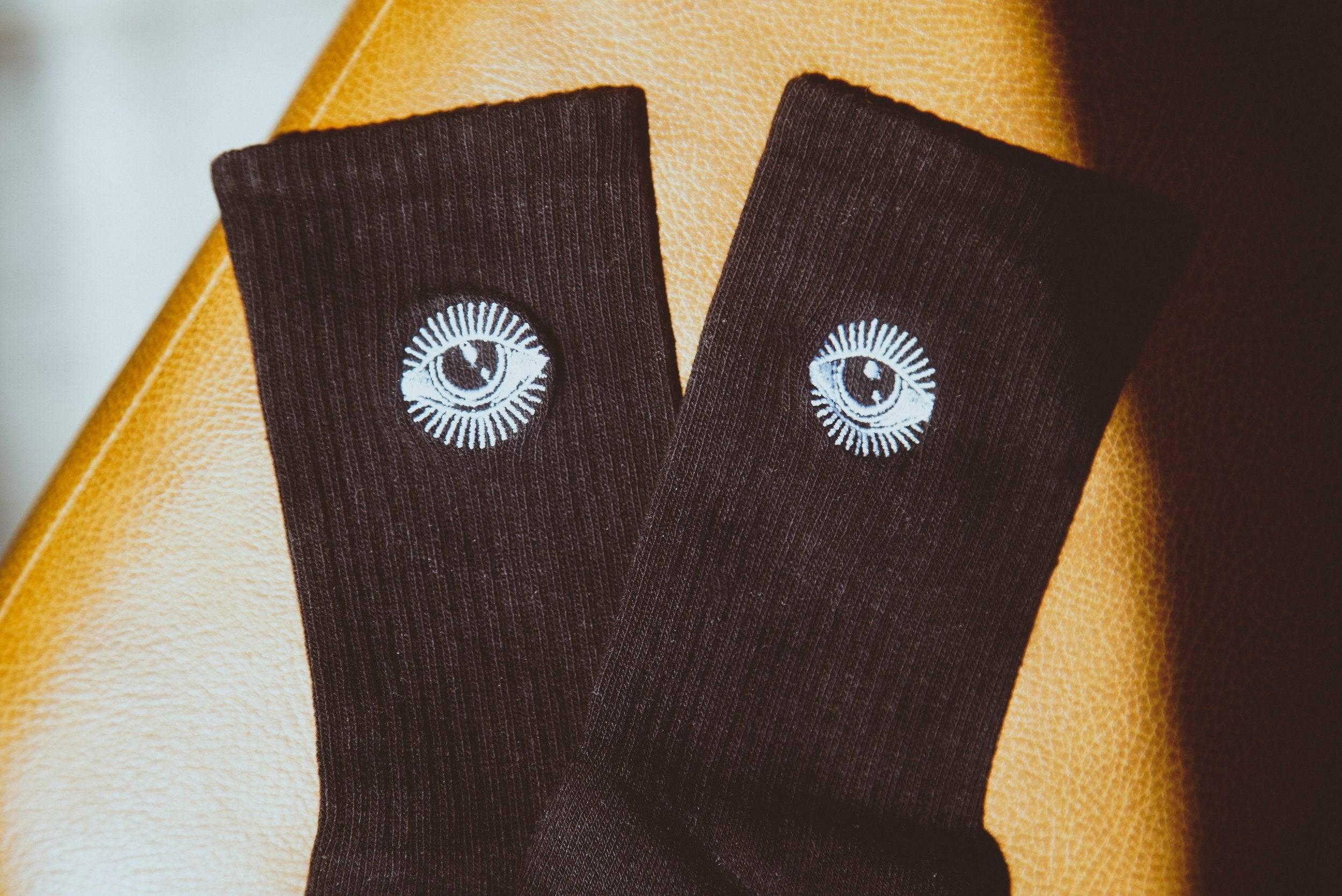 Black ribbed socks with white eye designs placed on brown leather surface