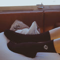 Person wearing black socks with eye design, resting legs on white pillow on brown couch
