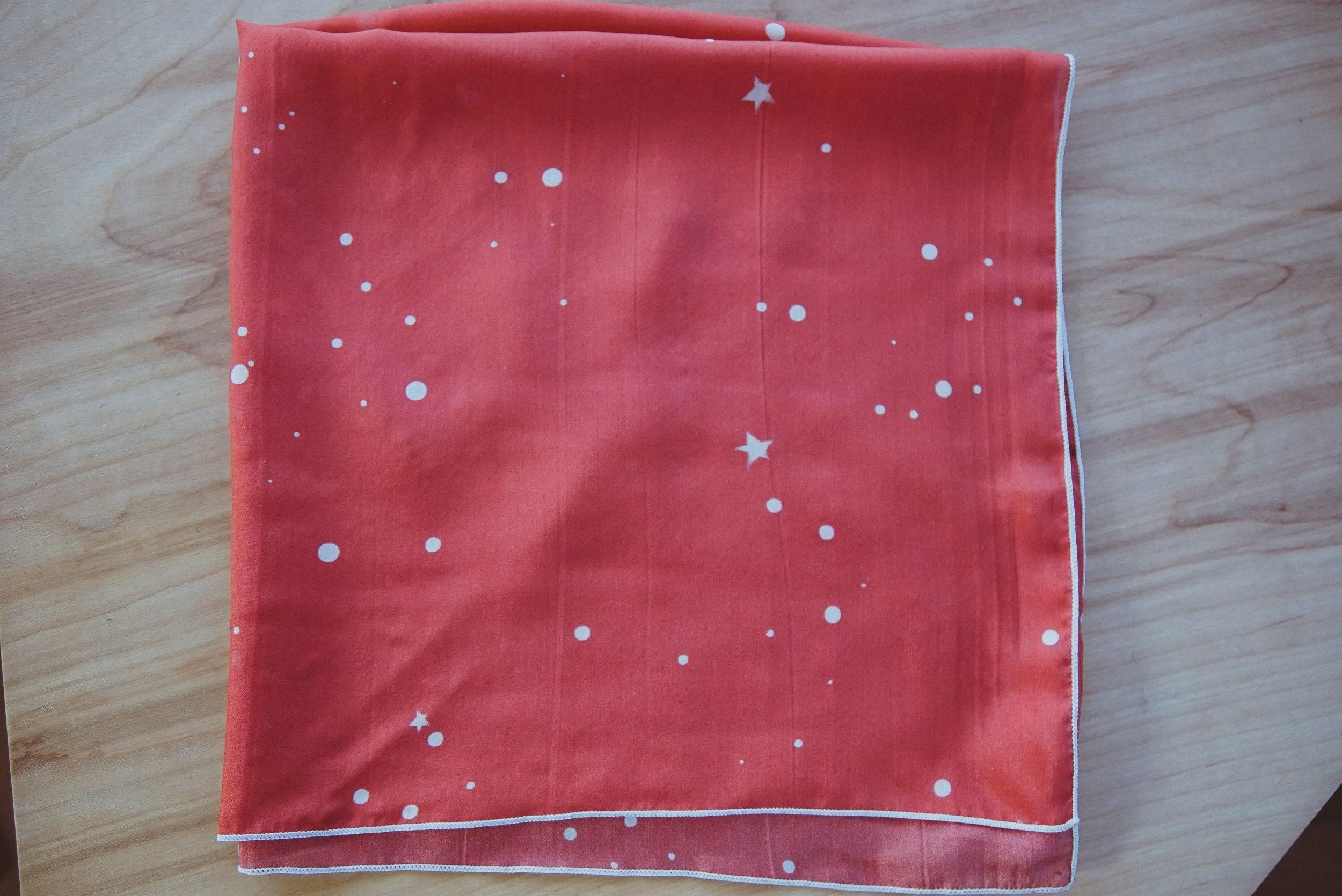 Coral pink fabric with white star and dot pattern, folded on wooden surface