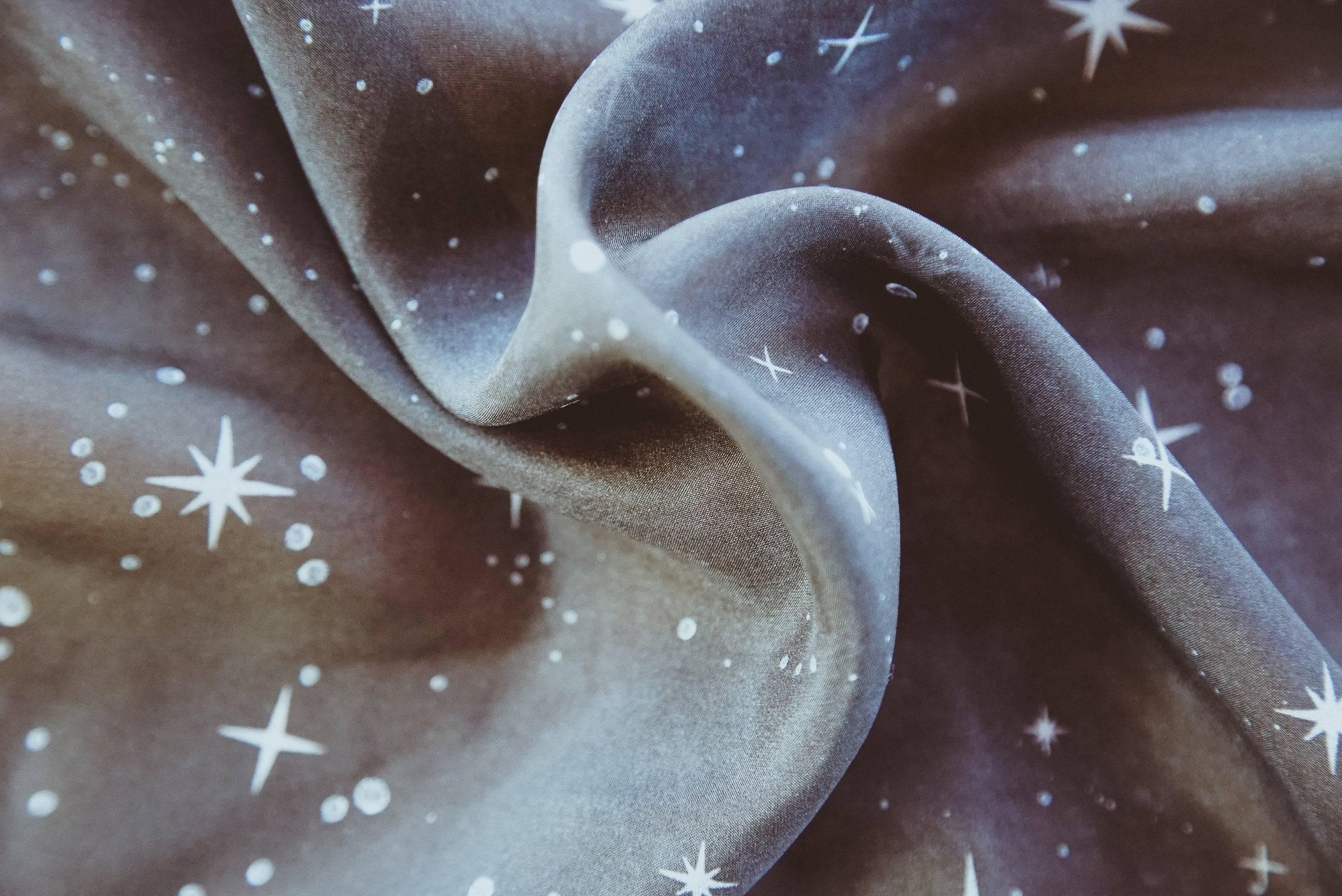 Close-up of soft gray fabric with white star and dot celestial pattern, folded and draped