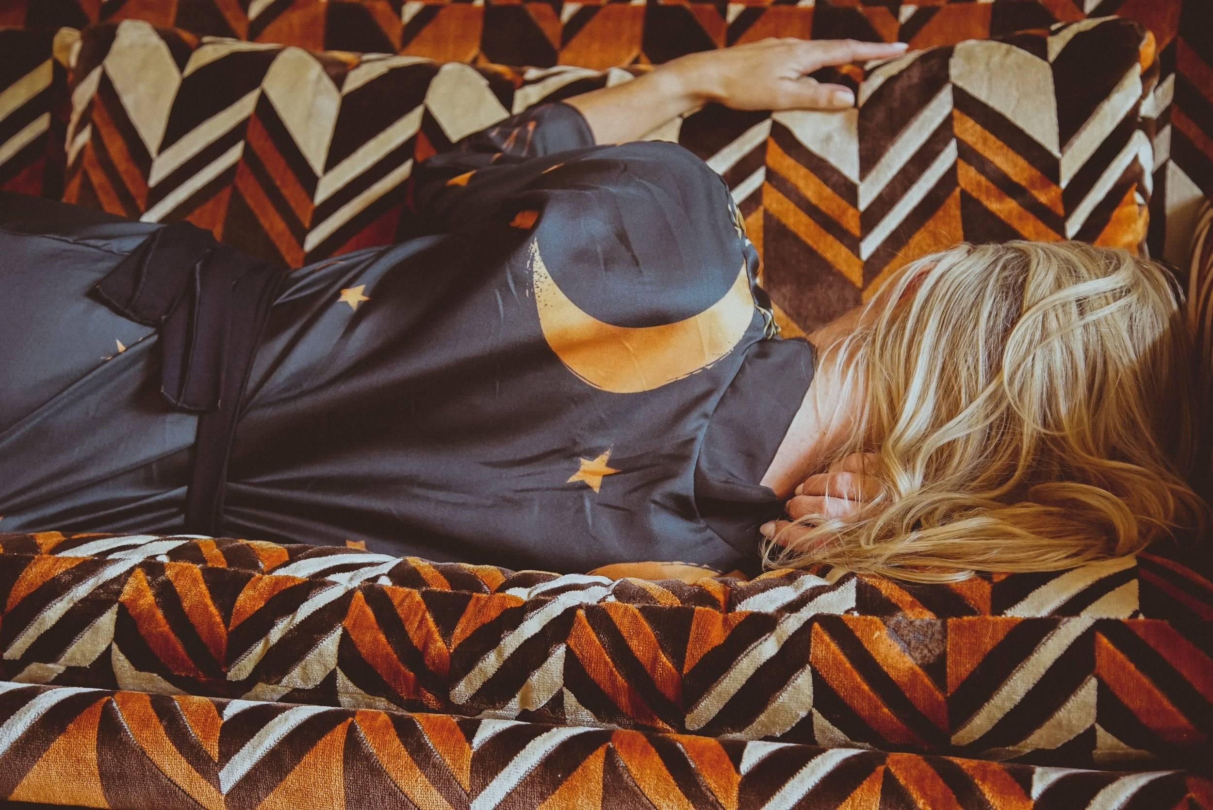 Person lying face down on patterned orange and brown sofa, wearing dark pajamas with moon and star design