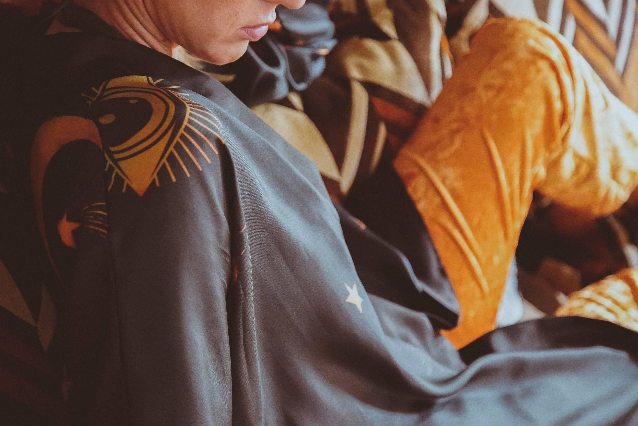 Person wearing a black shirt with yellow celestial designs and orange velvet pants sitting on a patterned couch