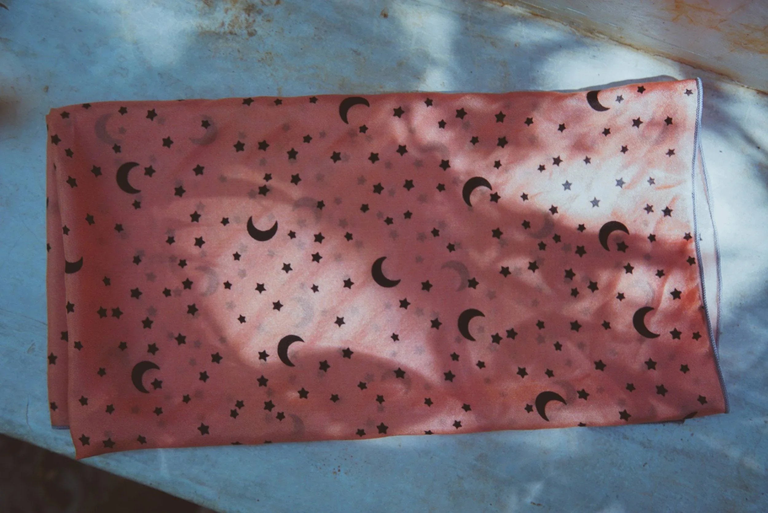 Pink fabric with black crescent moon and star patterns laid on a blue surface with shadows