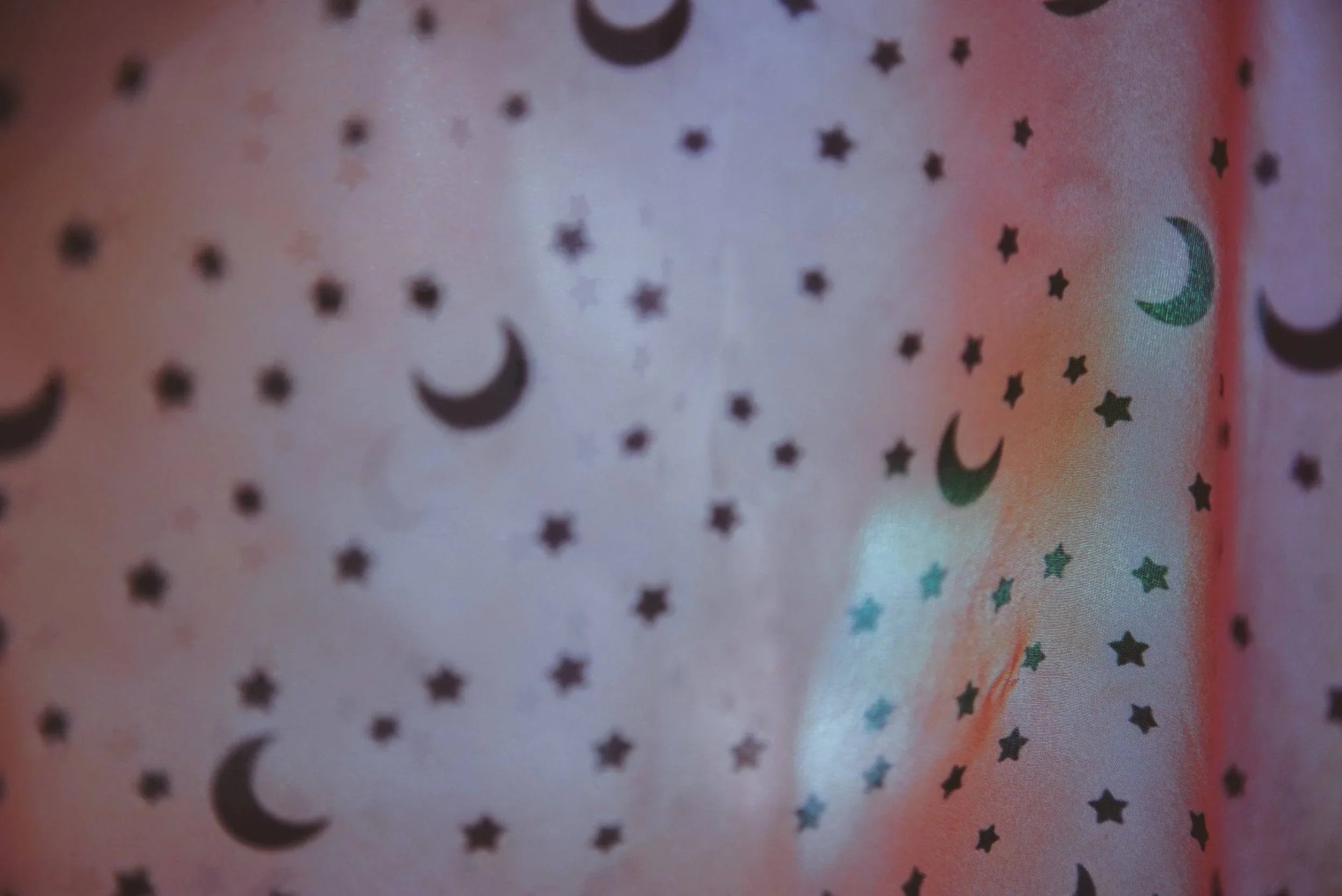 Close-up of fabric with black crescent moon and star patterns under soft, colorful lighting
