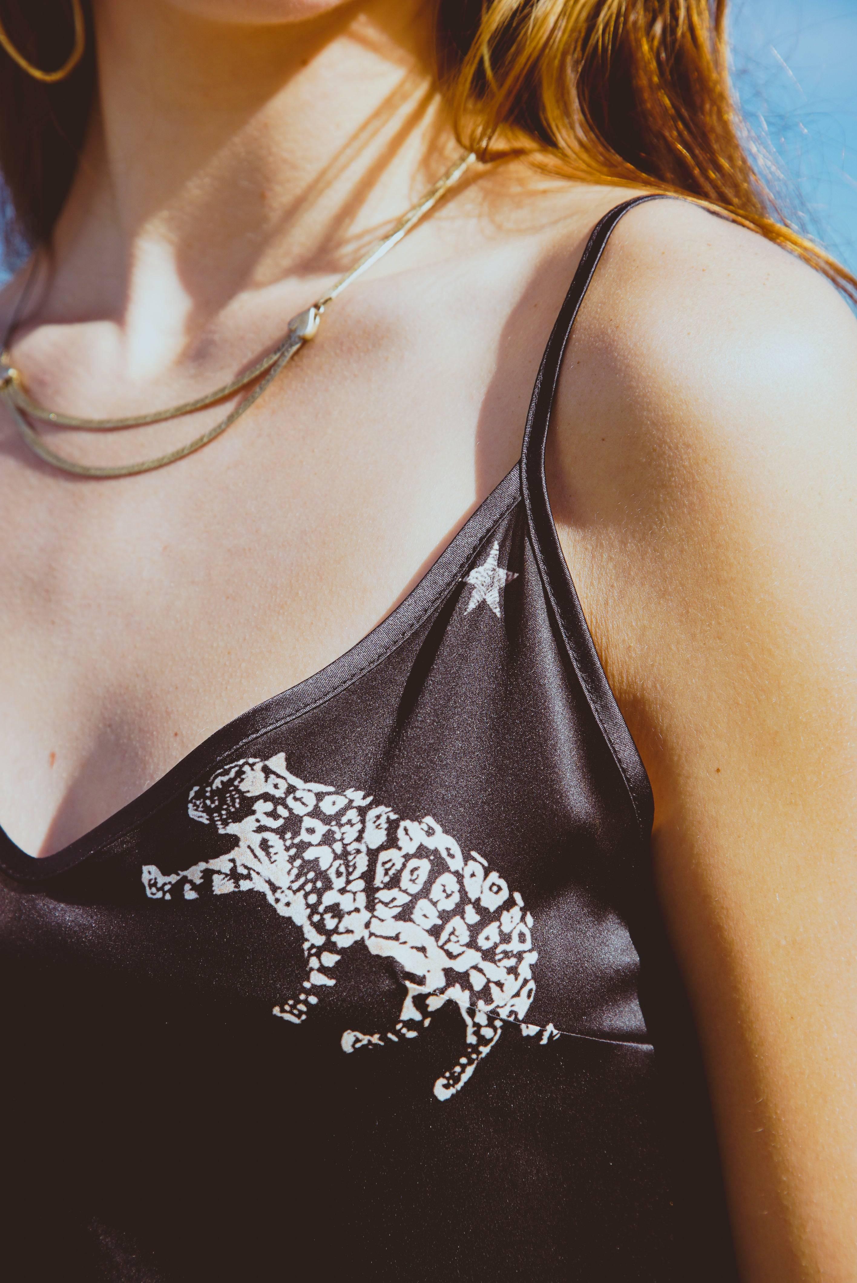 Close-up of woman wearing black camisole with white leopard print and star detail, gold necklace