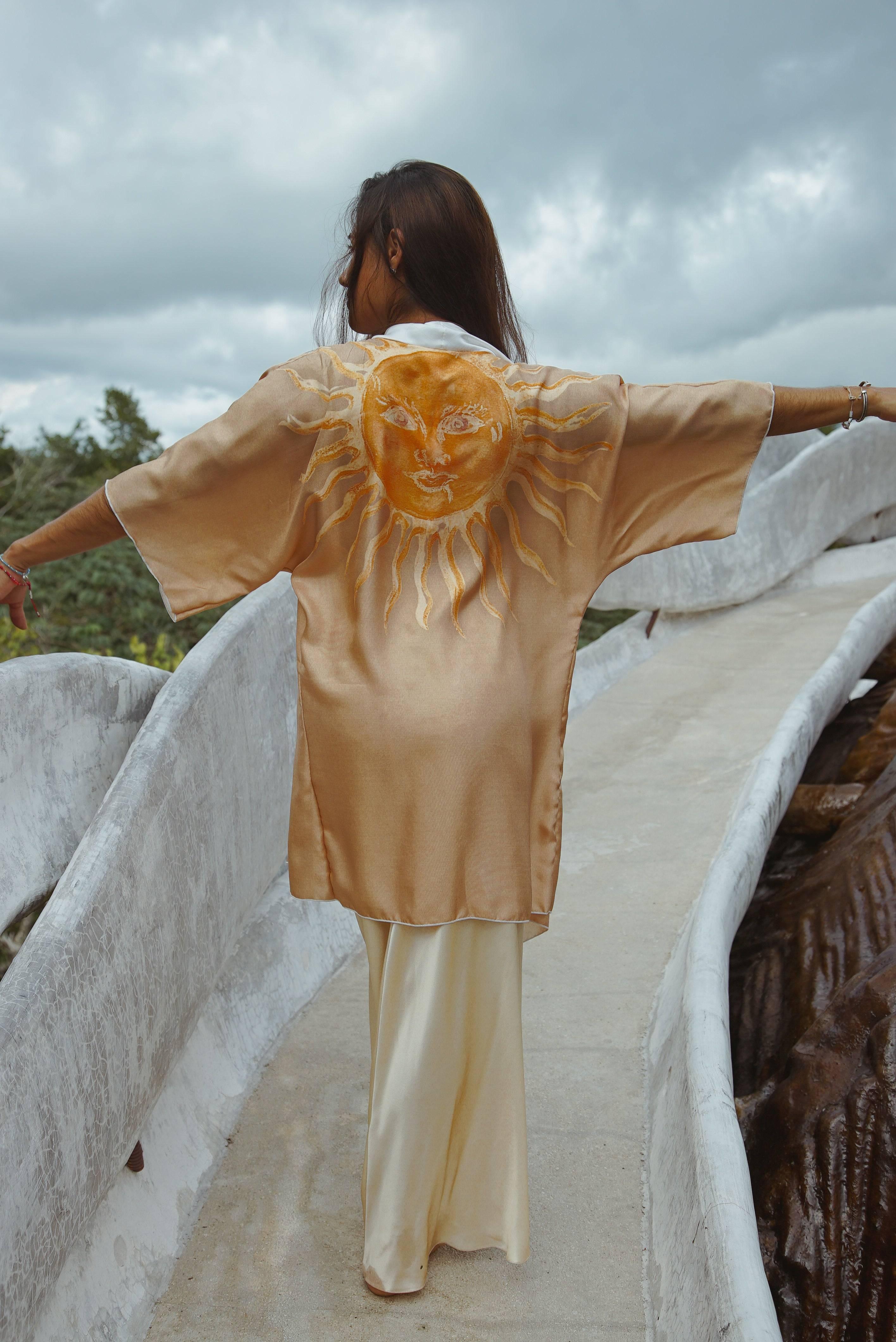 Woman walking on a curved concrete path wearing a golden kimono with a sun face design on the back